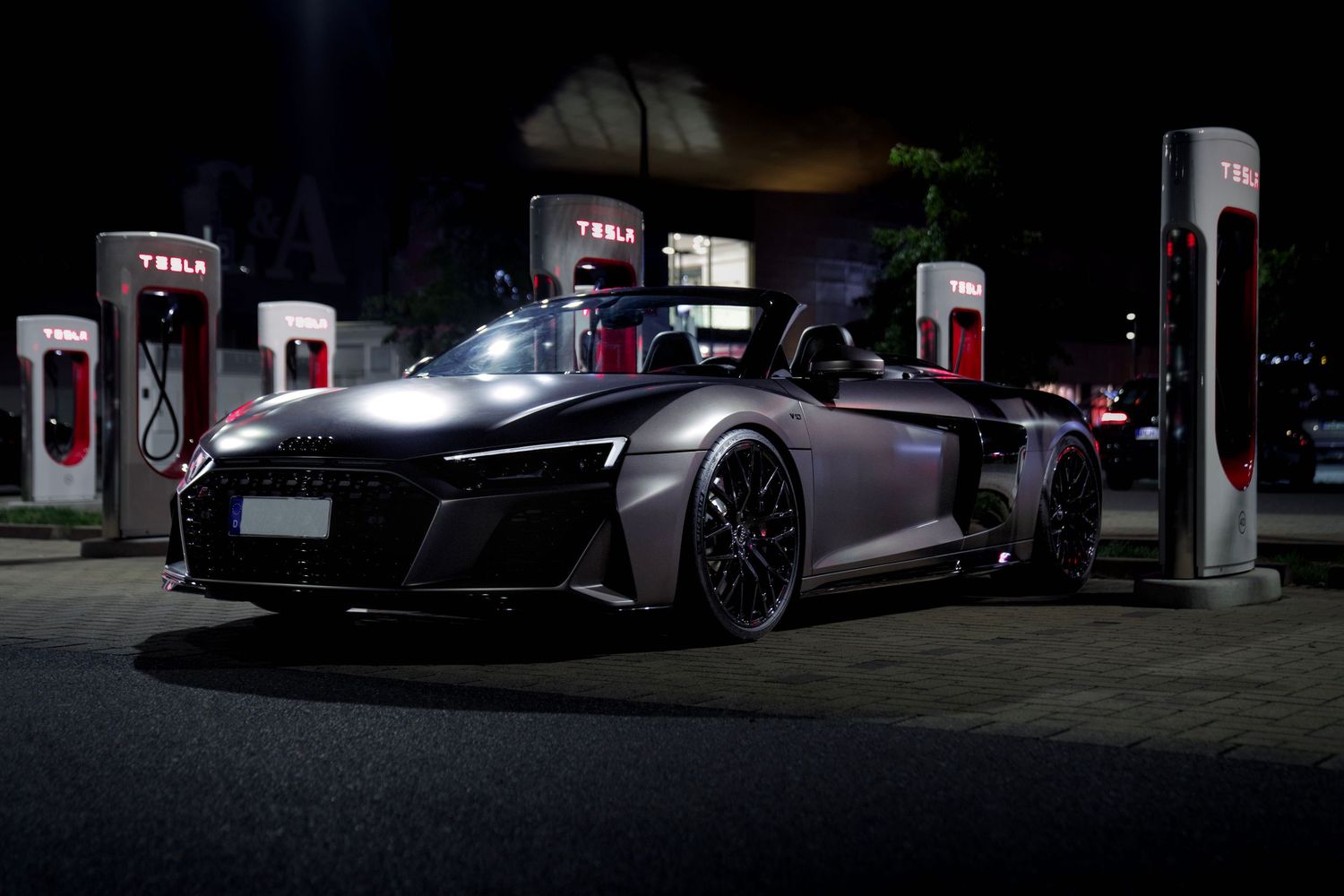 Dramatic nighttime shot of a modified Audi R8 at an electric vehicle charging station.