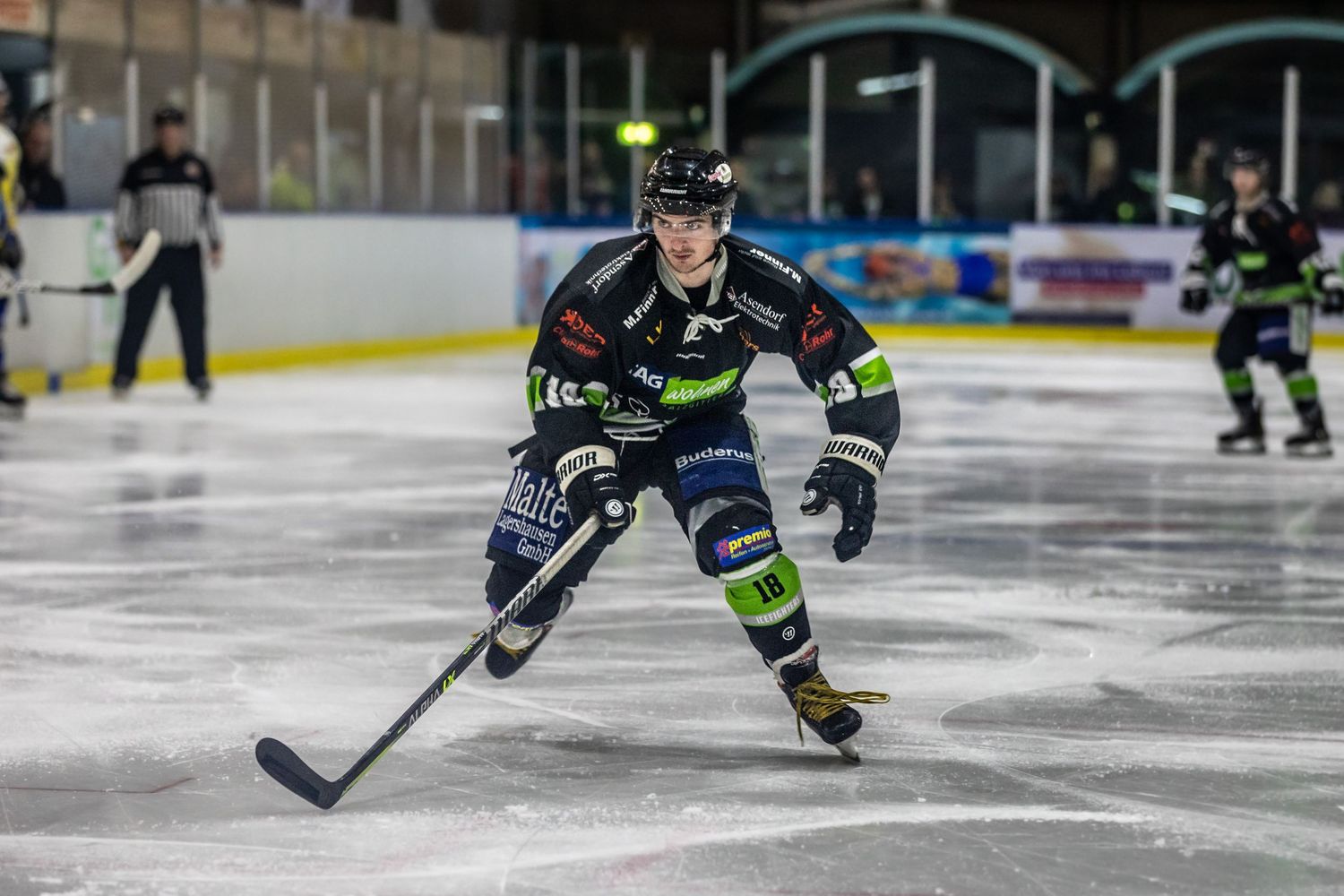Hockey player in black and green jersey skating with puck on ice rink.