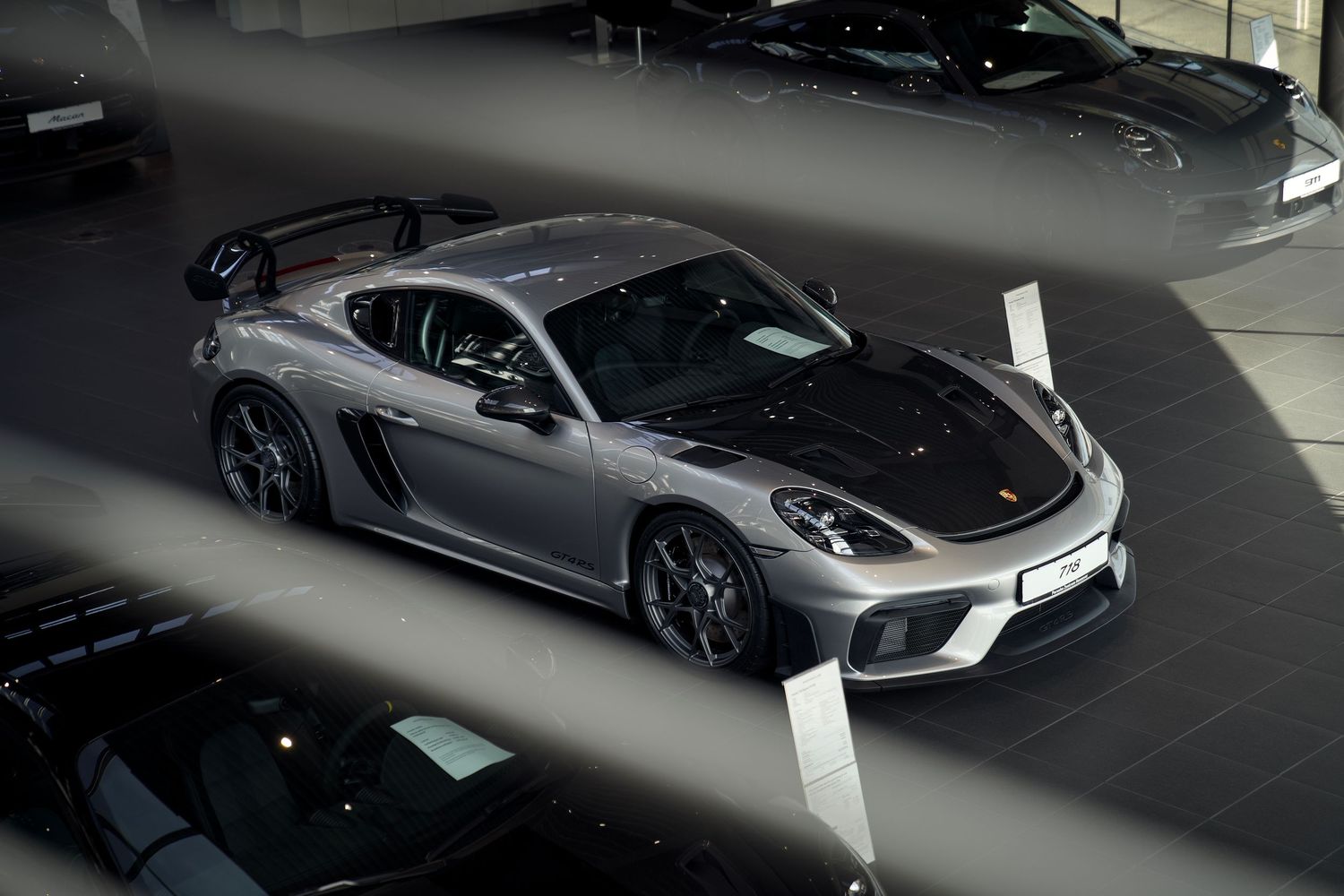 A sleek gray McLaren sports car is parked in a covered garage area with other luxury vehicles visible.