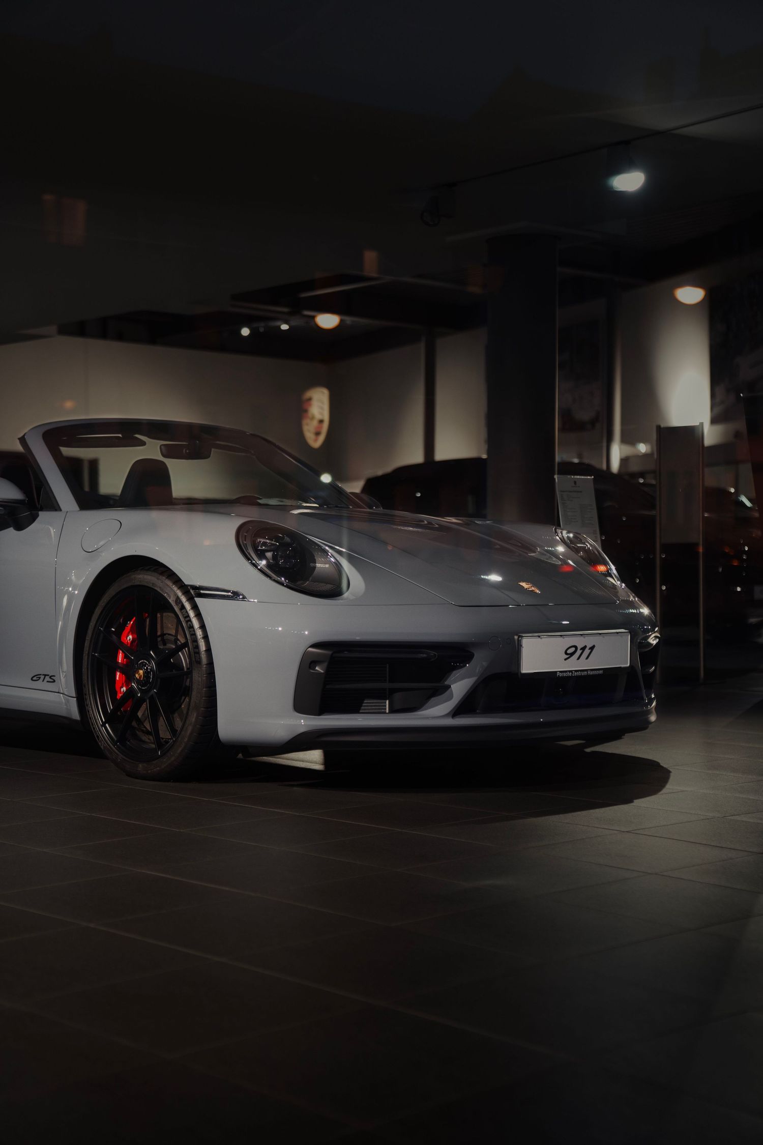 Silver Porsche 911 with red brake calipers displayed in a dimly lit showroom.