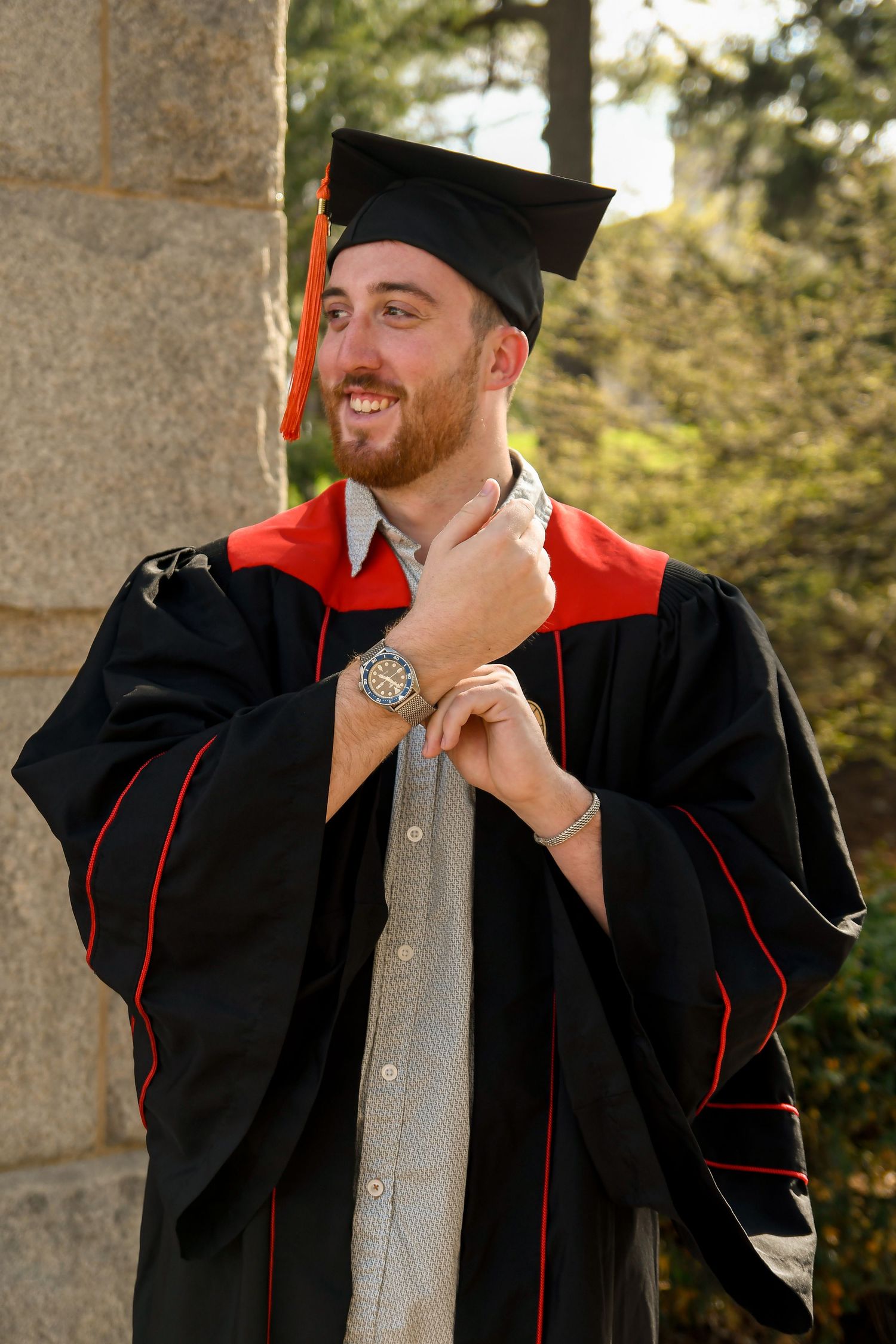 Male graduate in cap and gown looking away and playing with watch.