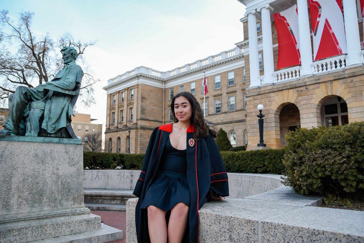 Girl sitting on ledge between statue and building