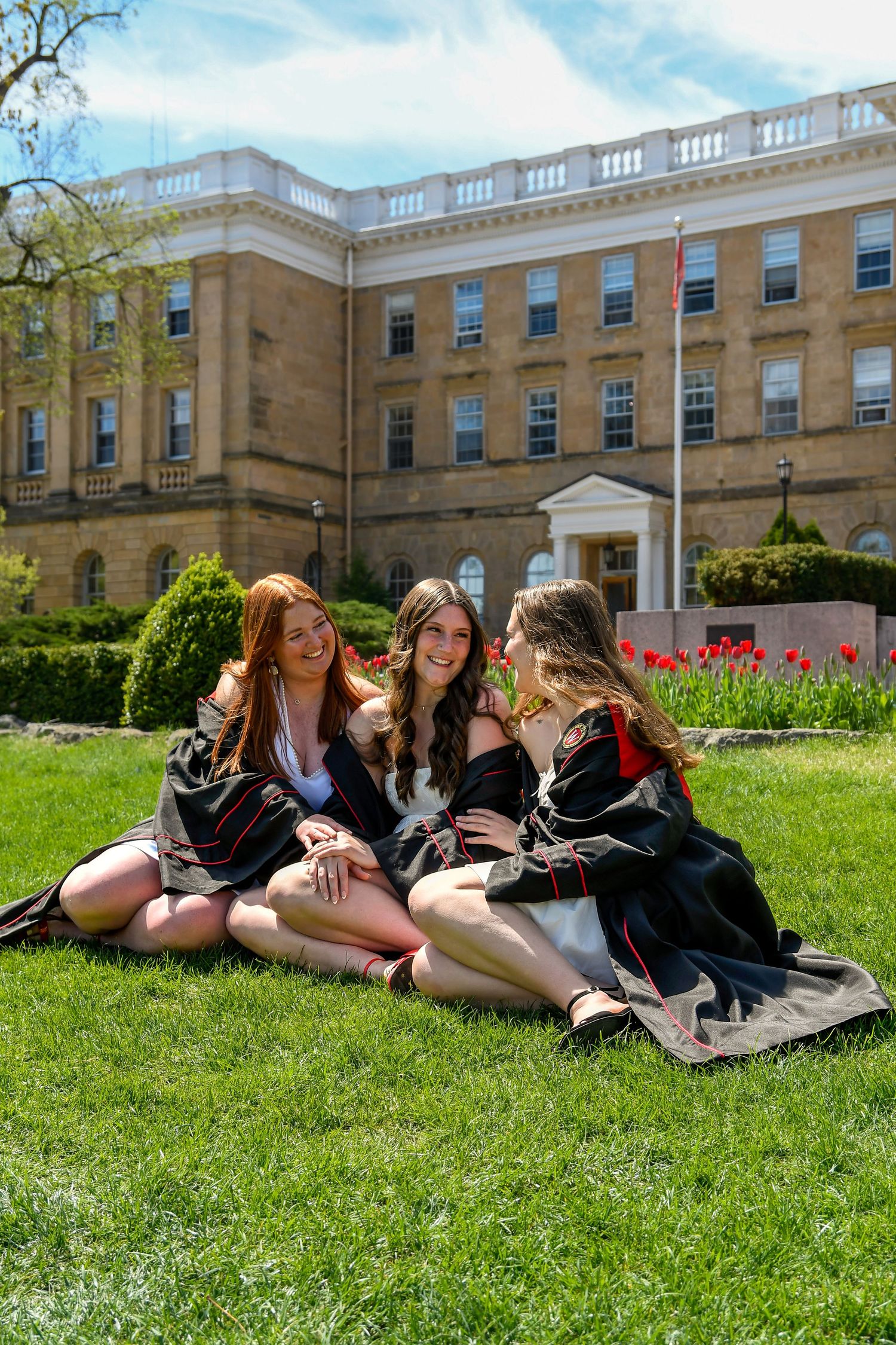 Three girls smiling at each other sitting on the grass