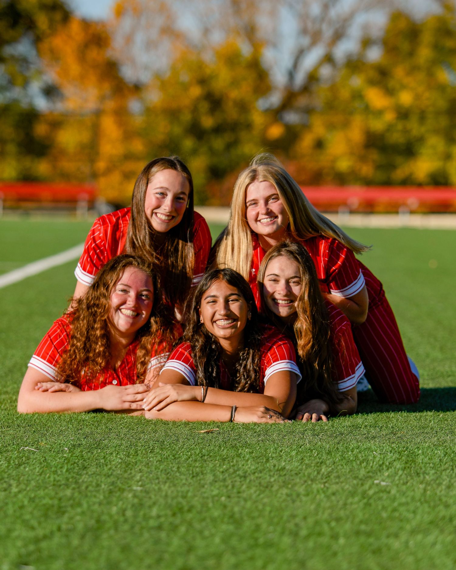 Group of five girls smiling while laying on the grass together in a pyramid formation