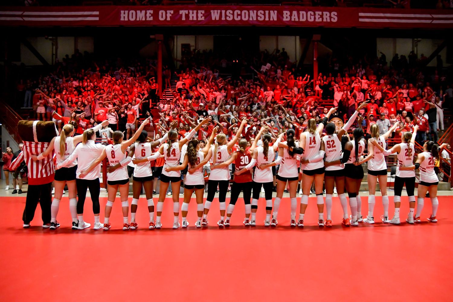 Volleyball team with their arms in the air looking at the crowd