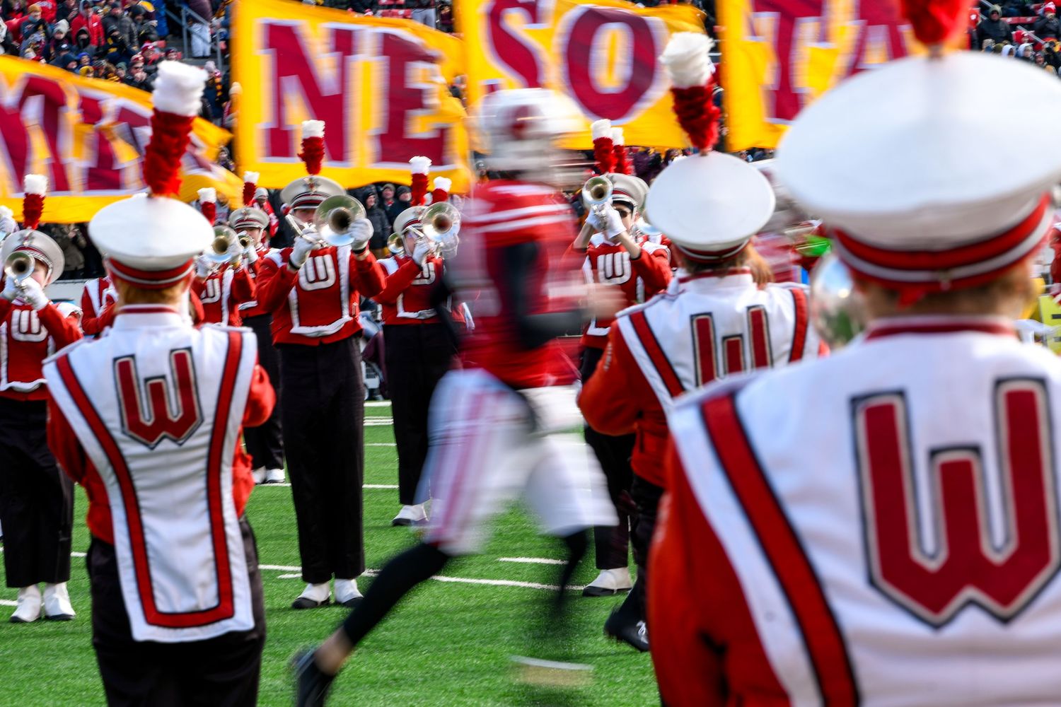 Football player runs through crowd on field where band is playing with 