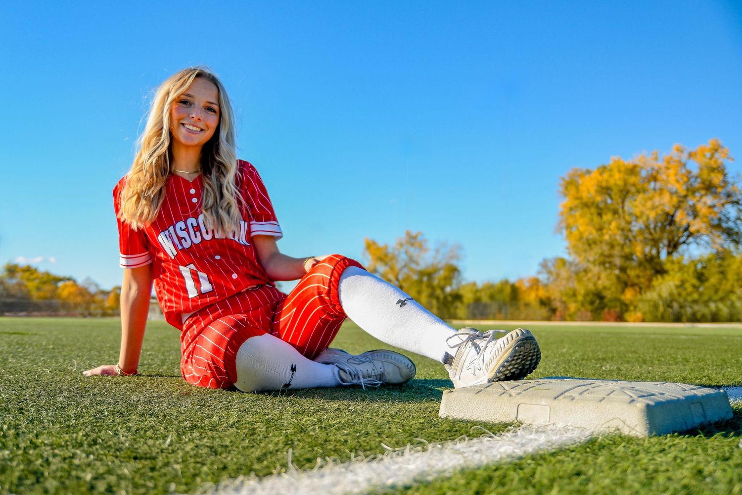 Girl smiling, sitting on grass with her foot on a baseball/softball base