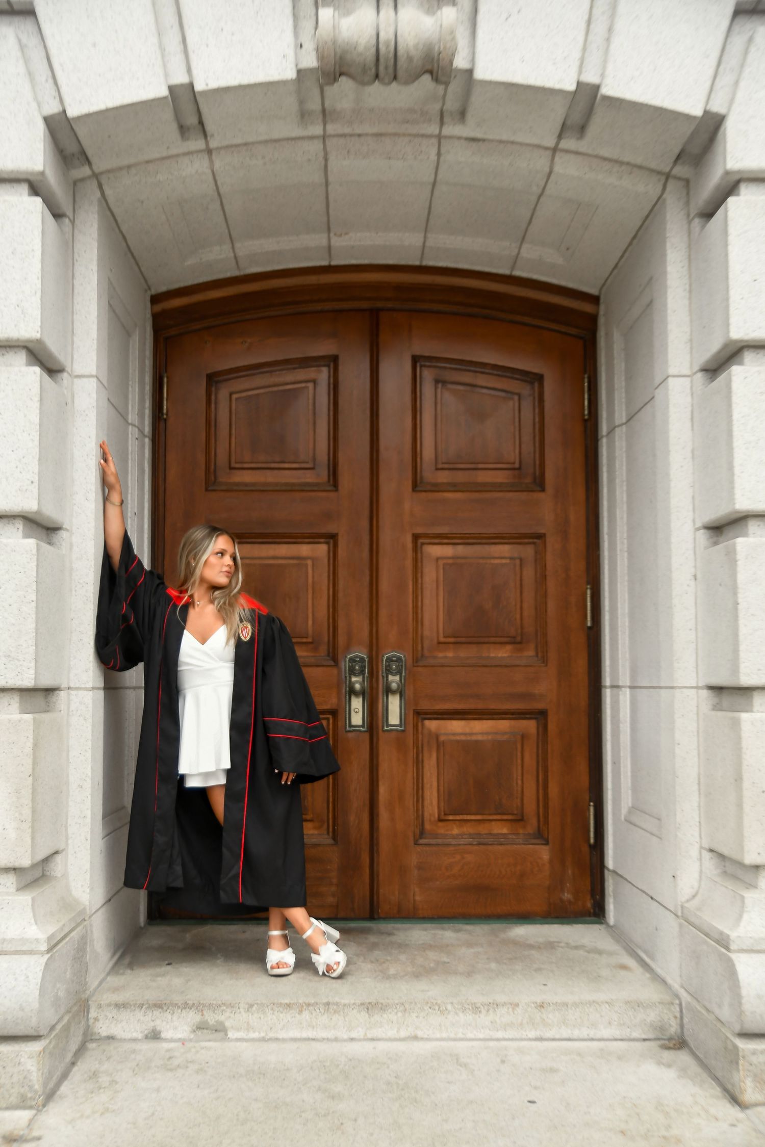 Girl in graduation gown leaning on wall looking away.
