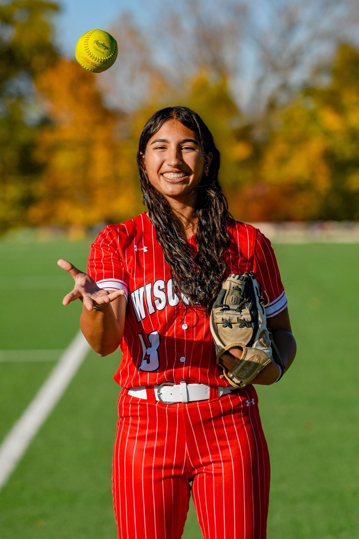 Girl smiling throwing a softball in the air and holding a glove