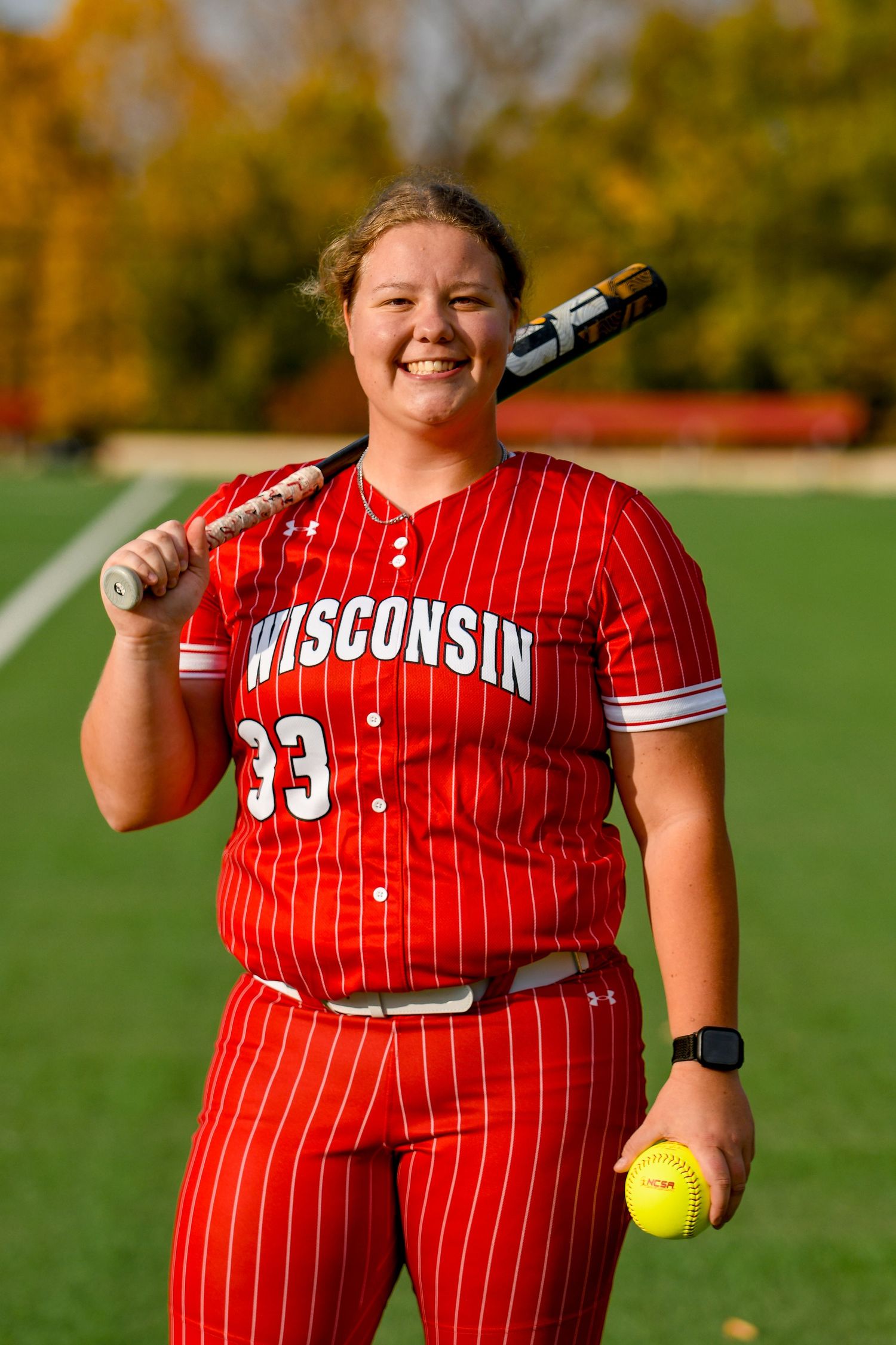 Girl smiling holding a softball and bat in uniform