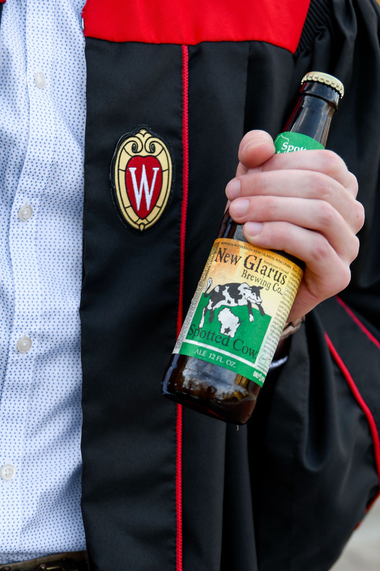Student holding a beer wearing their graduation gown.