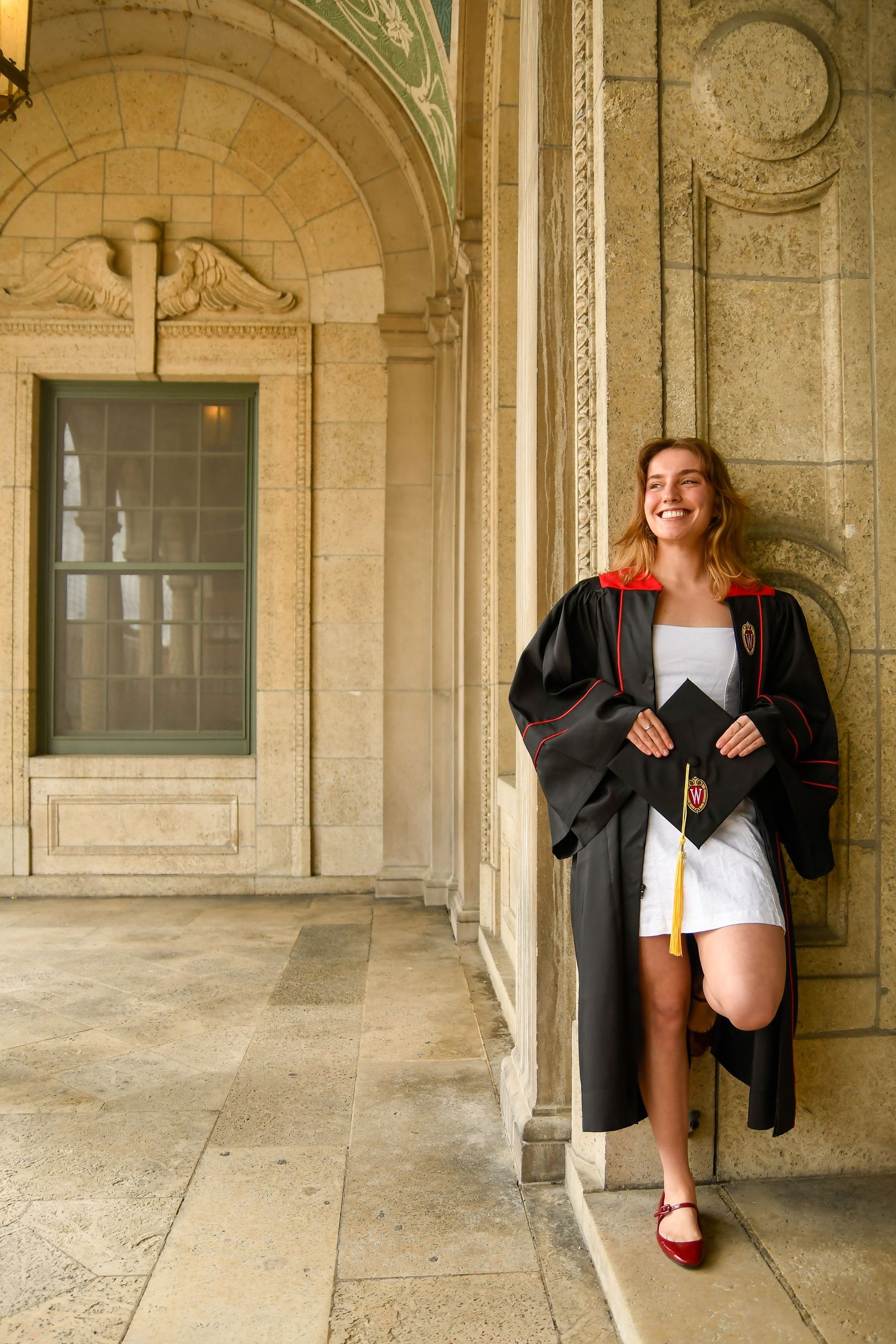 Girl in graduation gown holding cap looking away.