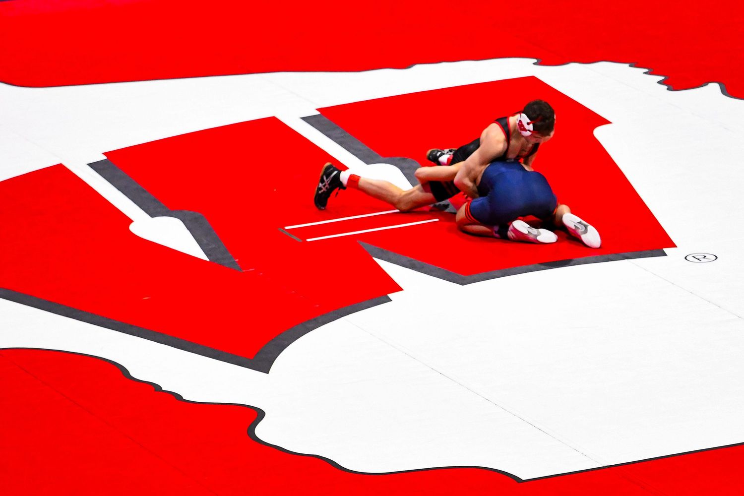 Wrestlers pictured from above wrestling on a Wisconsin branded mat