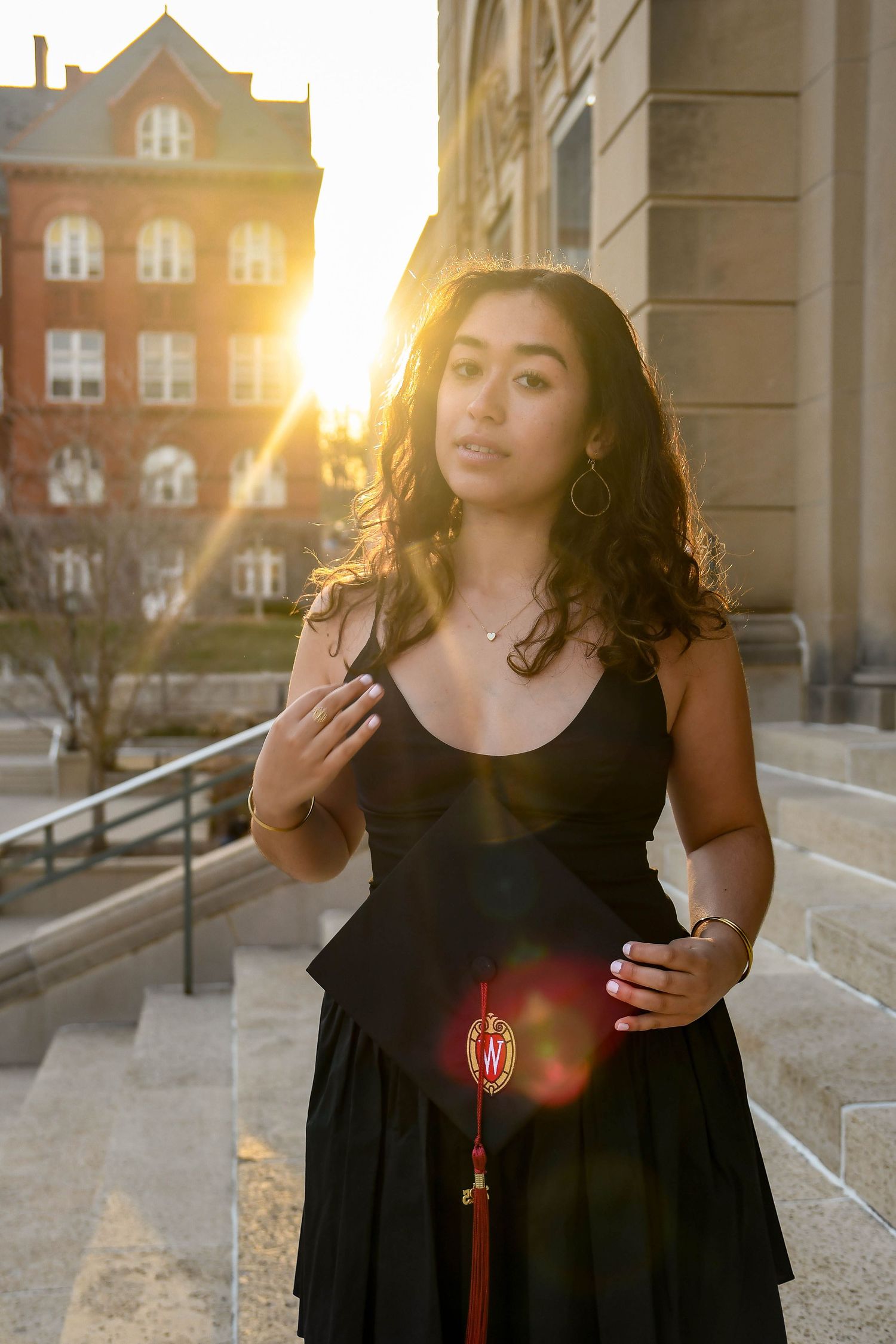 Girl at sunset holding her graduation cap and pulling her hair