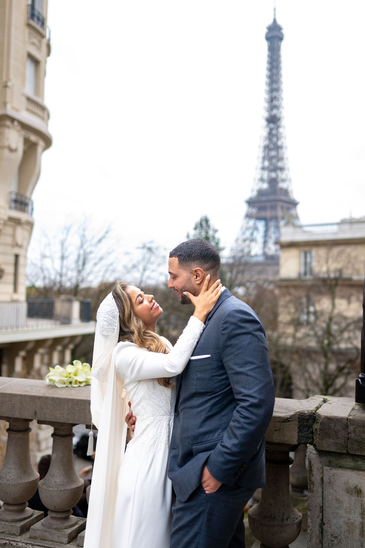 Romantic couple sharing intimate moments on a Paris balcony with the iconic Eiffel Tower visible in the background.