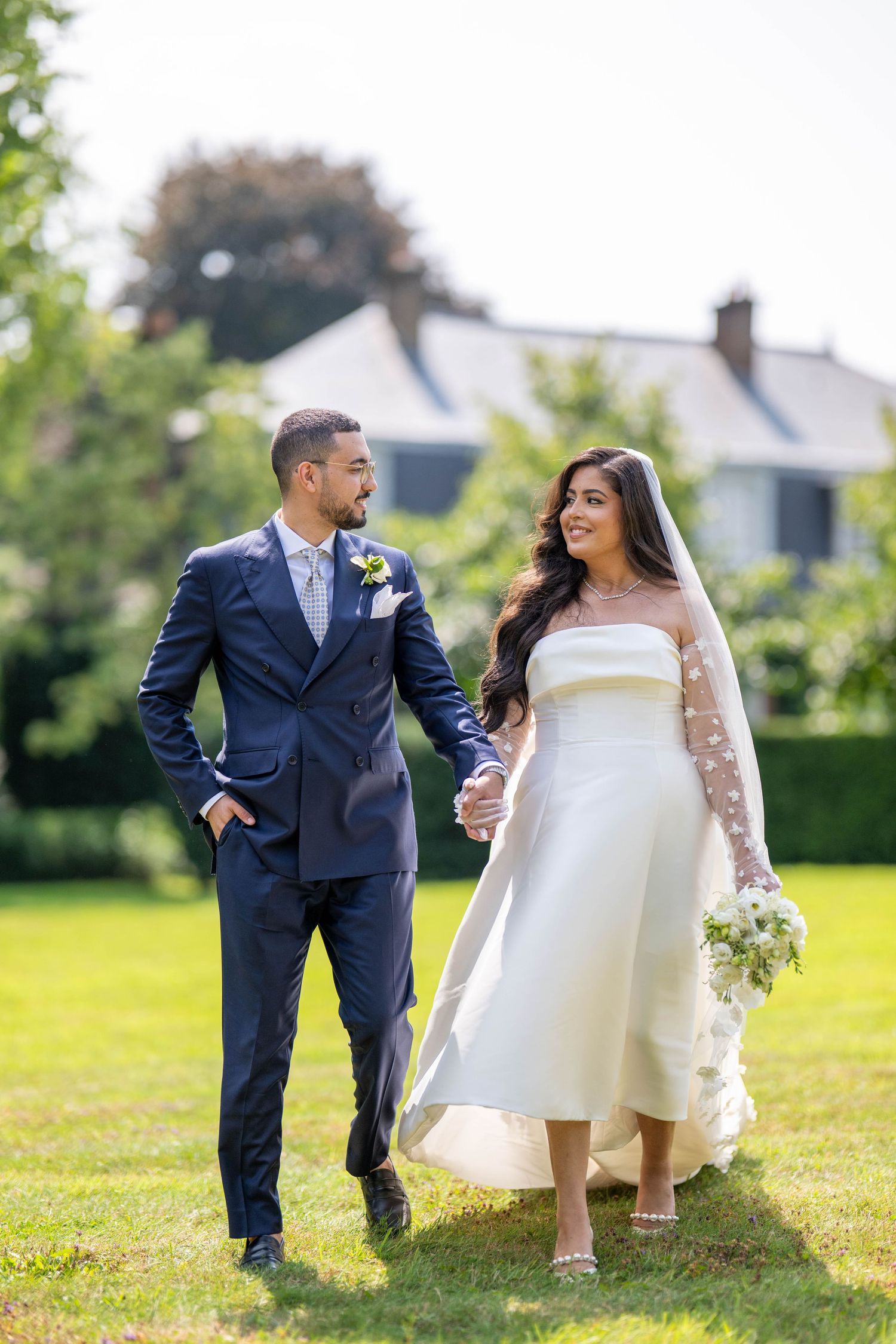 A couple in wedding attire share playful moments together on a sunny lawn during their outdoor photo session.
