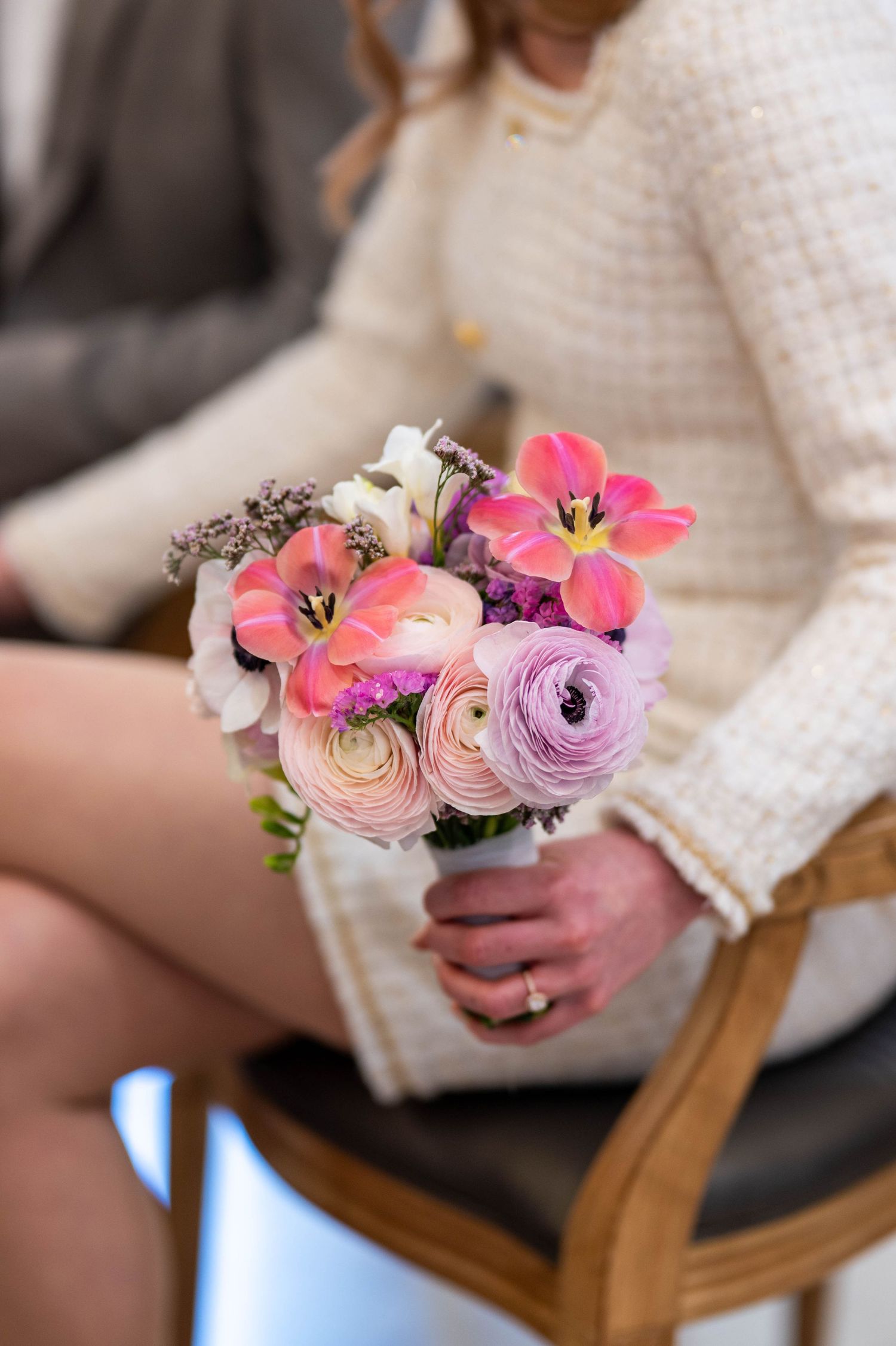 Delicate spring bouquet with pink tulips and purple ranunculus flowers on wooden chair.