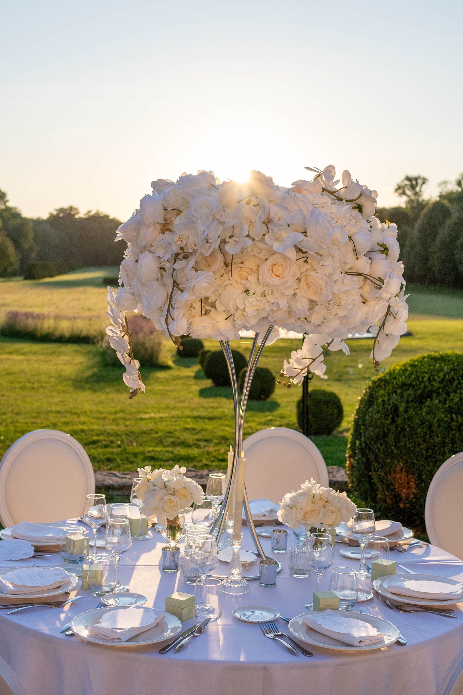 Elegant white orchid centerpieces adorn round dining tables set for a luxurious outdoor wedding reception at sunset.