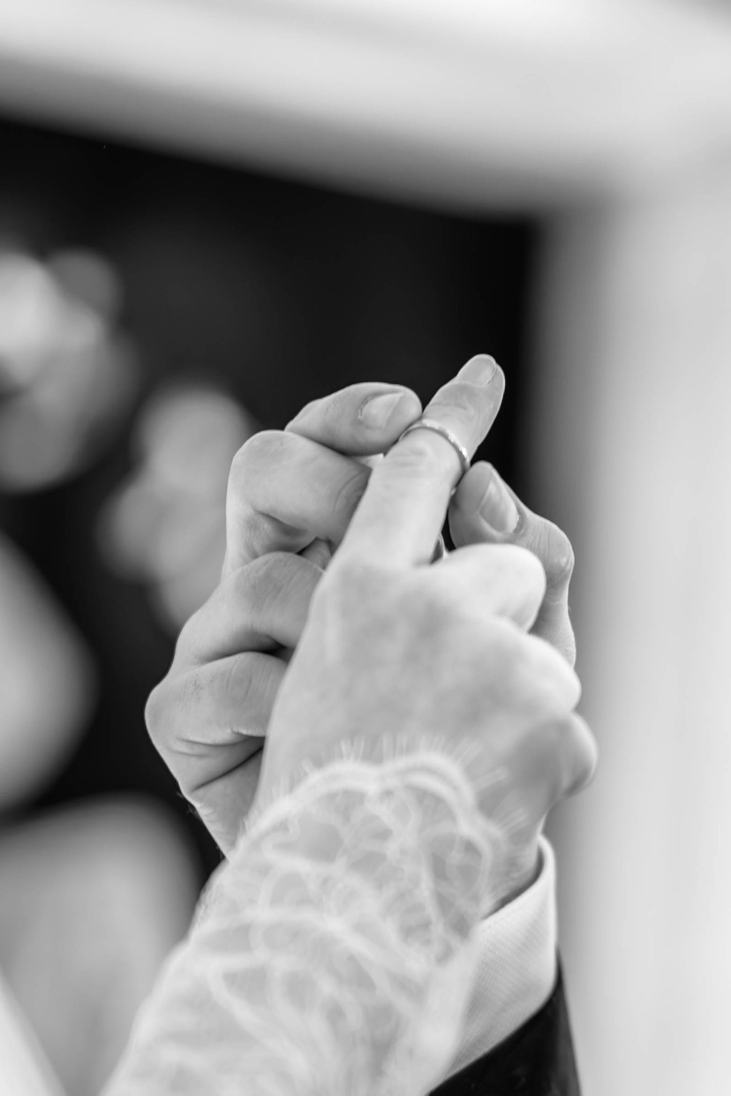 A close-up black and white photograph shows two hands clasped together with delicate white lace details.