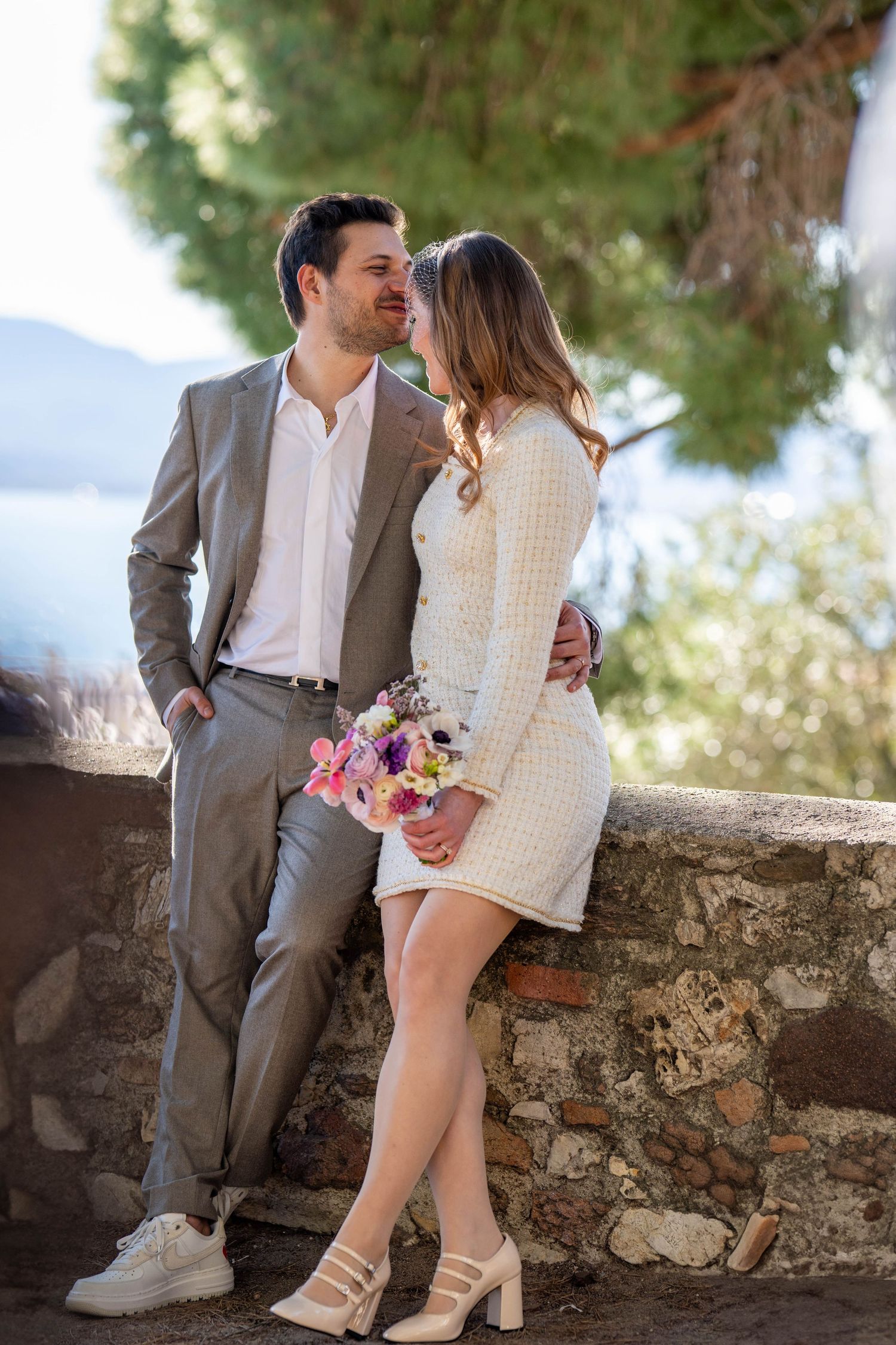 Romantic couple sitting on stone wall with colorful bouquet in outdoor garden setting.