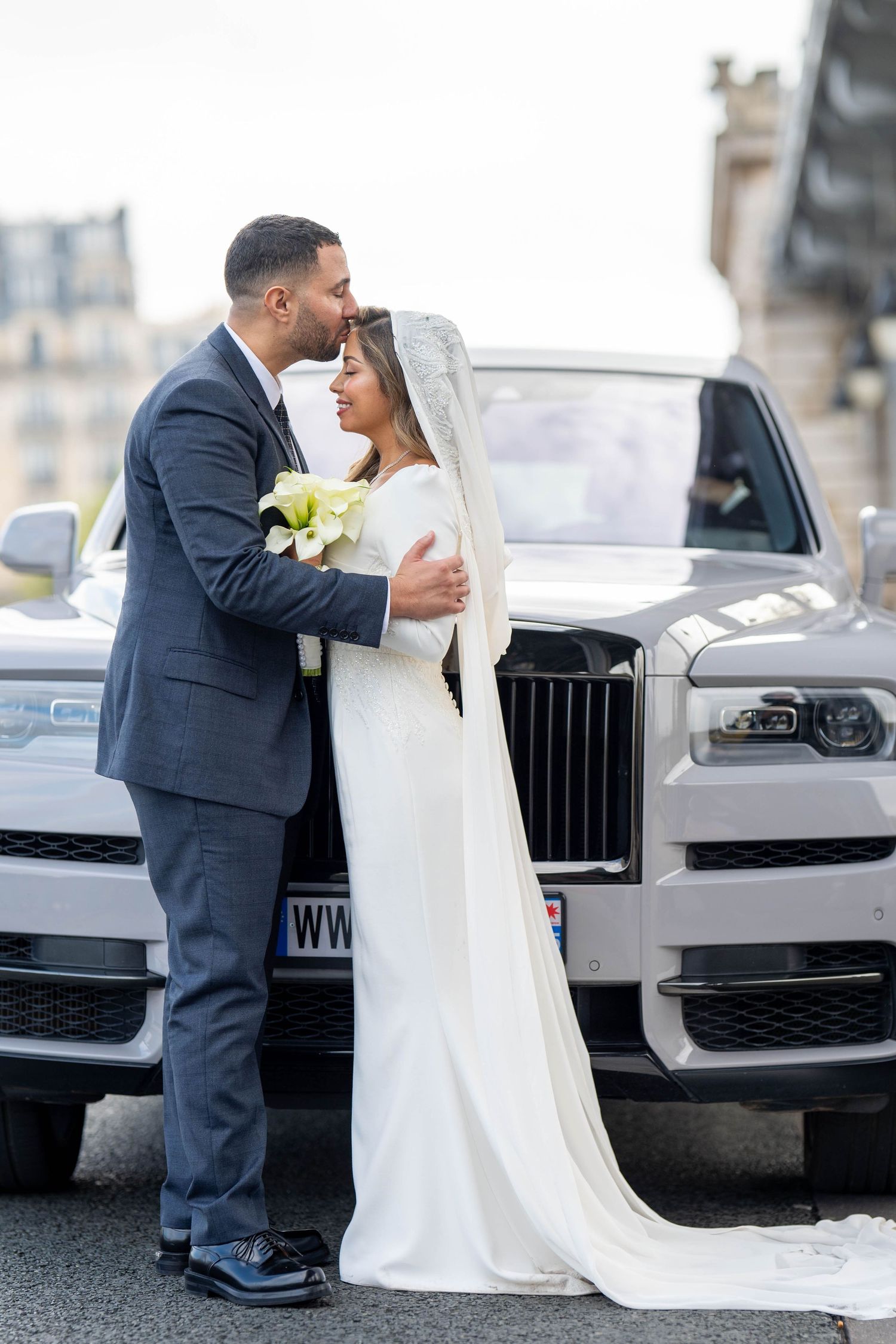 A luxury white Rolls Royce serves as backdrop for wedding photos near historic architecture.