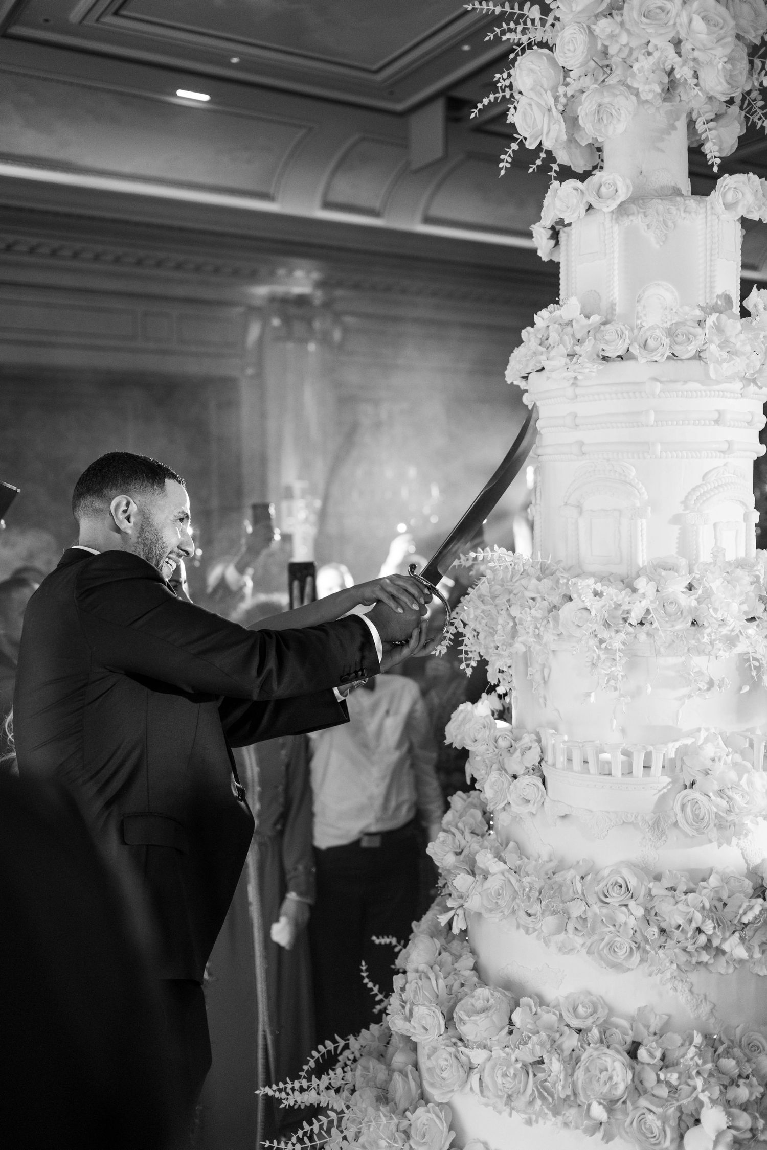 Wedding couple cutting into an elaborate multi-tiered white wedding cake at their reception.