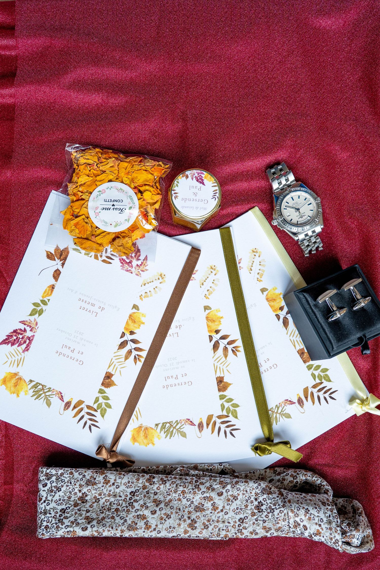 Wedding invitation suite with floral designs in orange and burgundy tones laid out on red fabric.