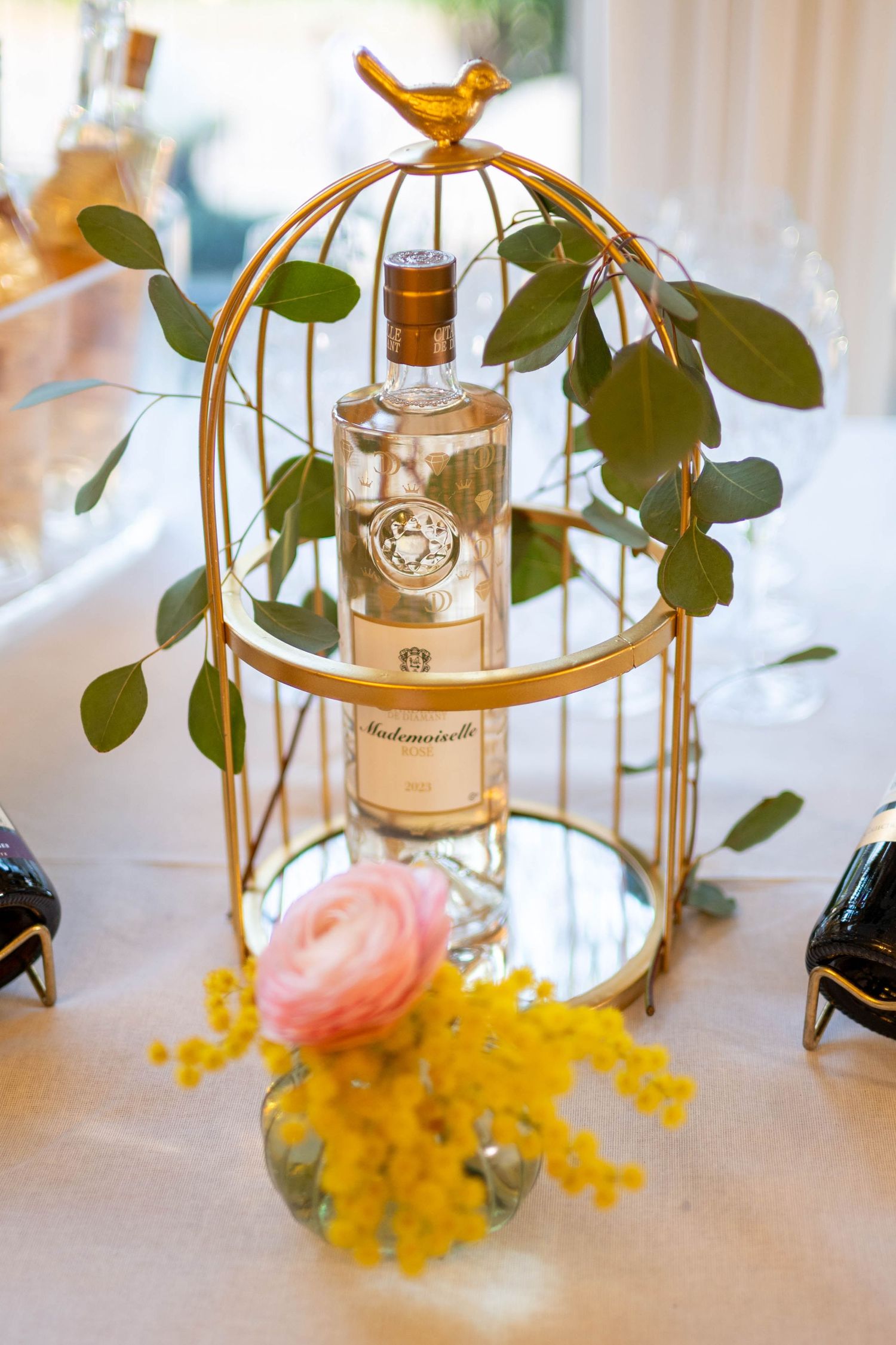 Elegant table decor featuring gold lanterns, yellow mimosa flowers, and eucalyptus leaves.