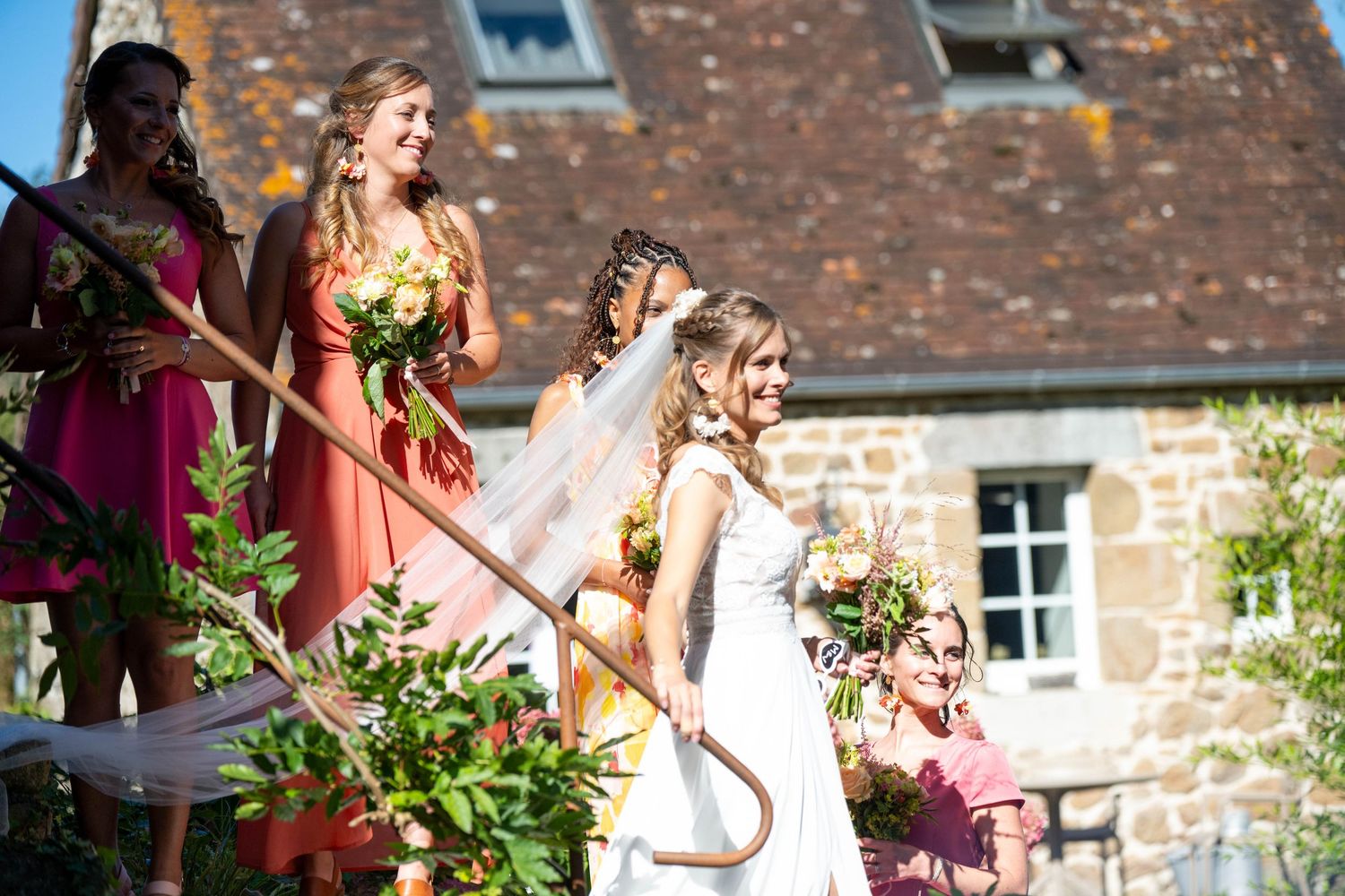 Wedding party walking through garden path with brick building in background.