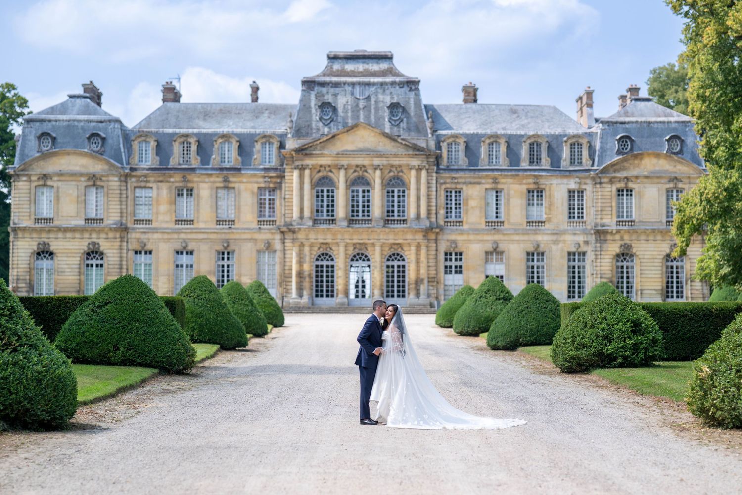 Panoramic view of a grand French chateau with elegant architecture and manicured gardens in daylight.