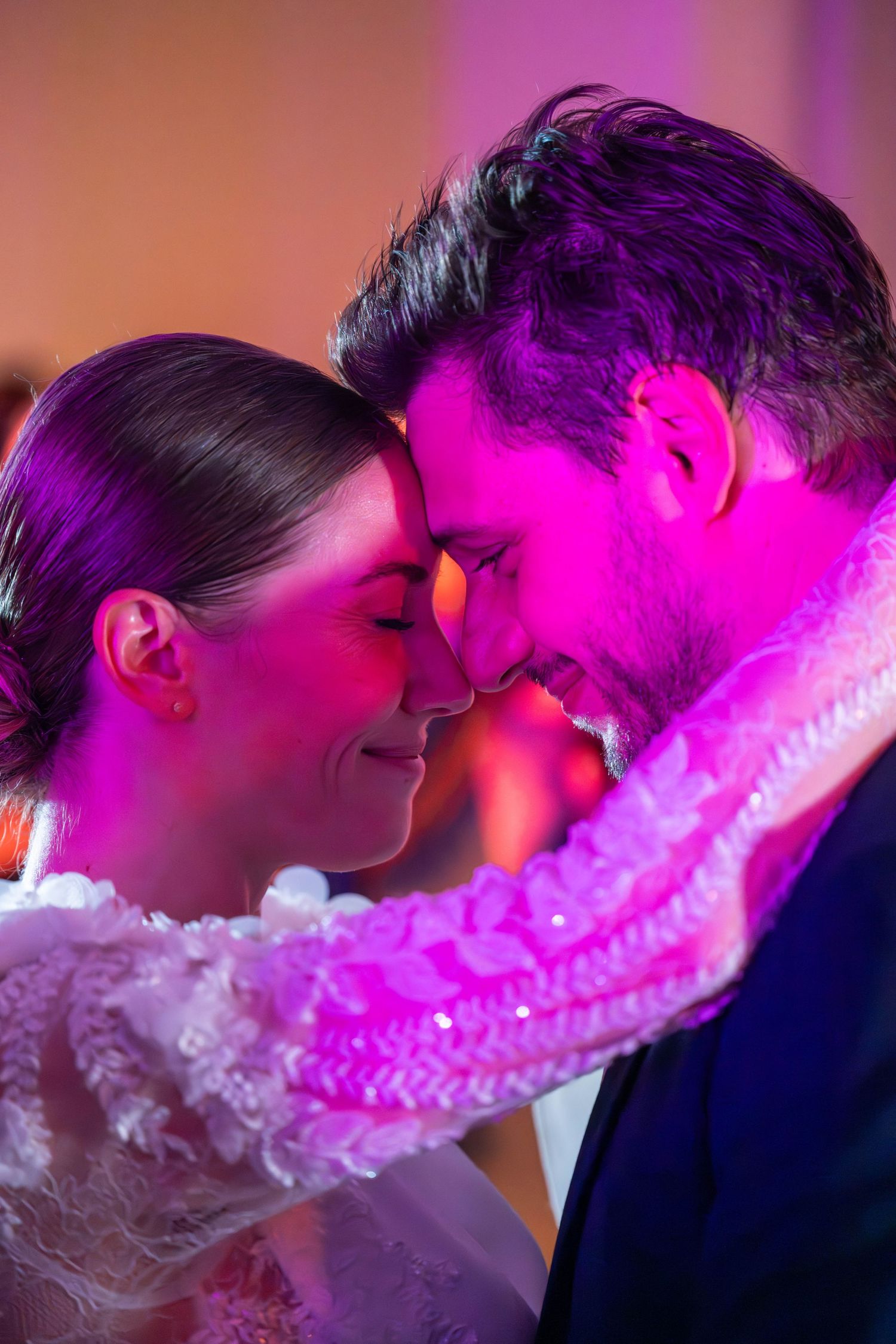 A romantic couple shares a kiss under vibrant pink lighting while vapor or smoke creates a dreamy atmosphere.