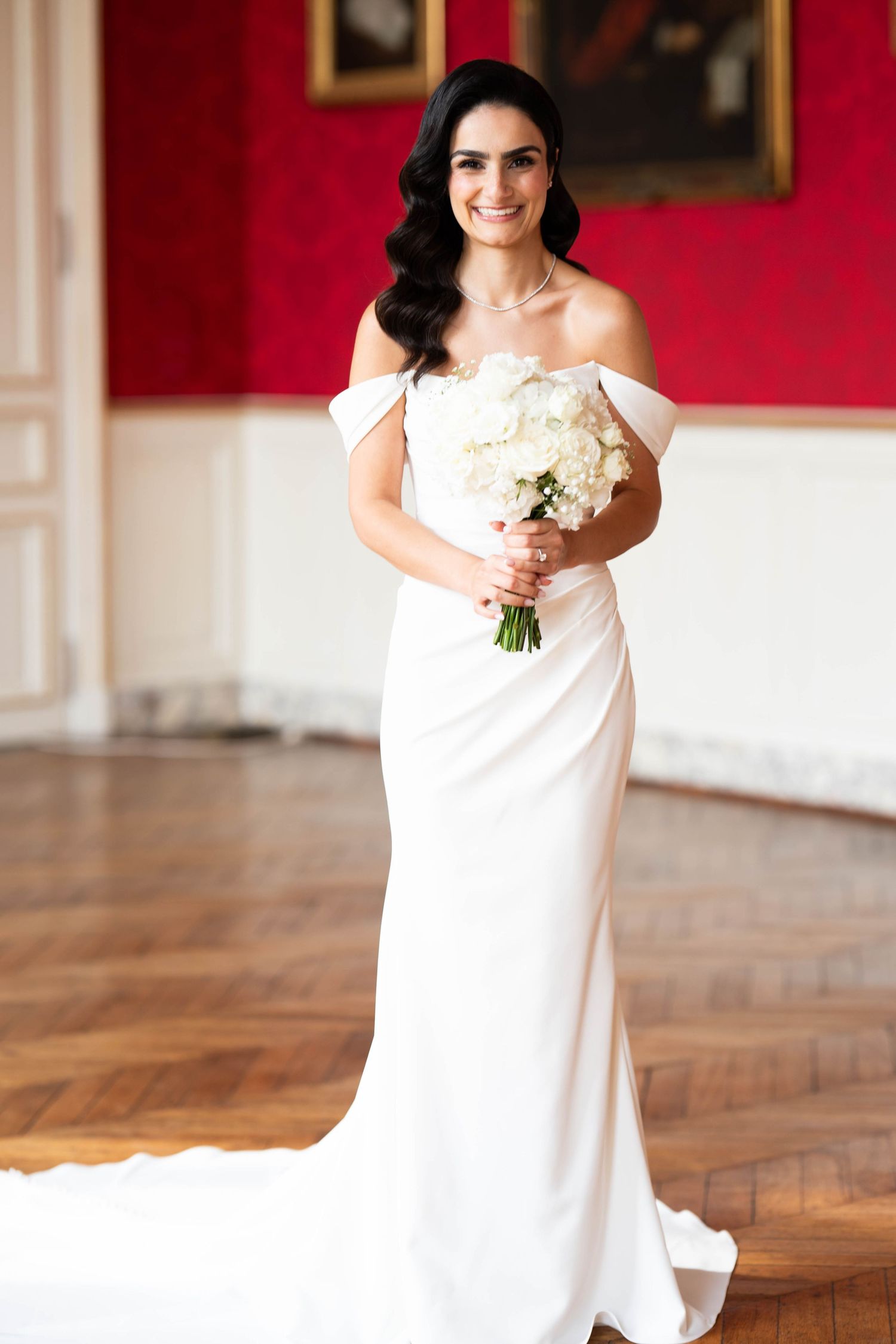 Classic white sleeveless wedding dress shown in an elegant room with red walls.