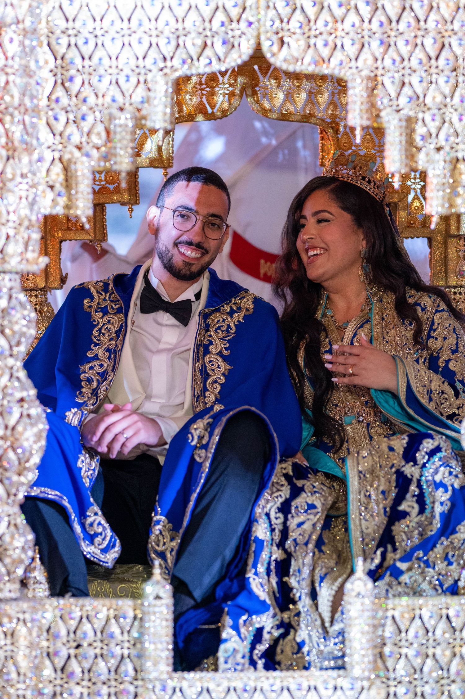 A couple in elegant blue and gold formal attire share a joyful moment during a special celebration.