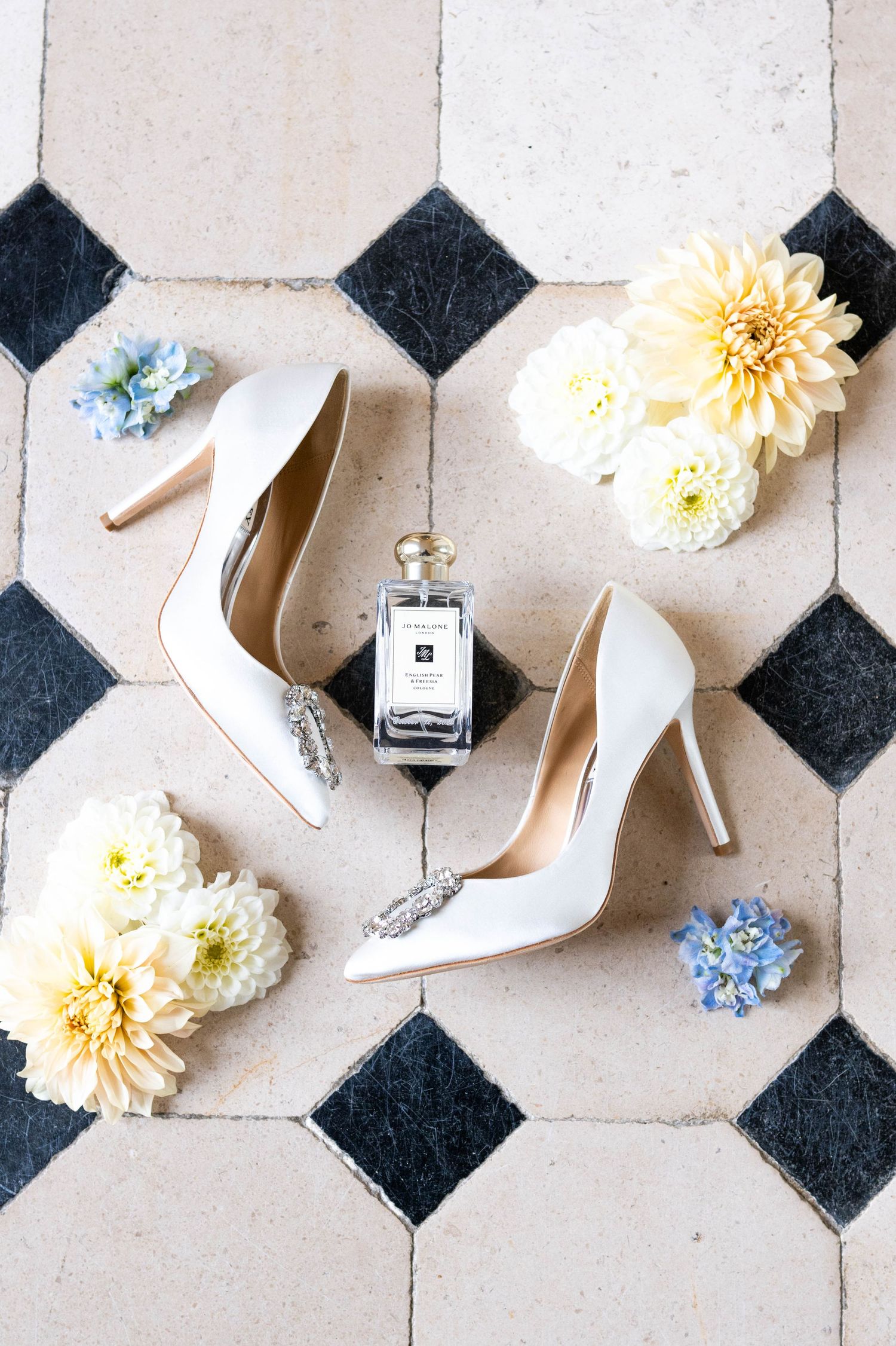 White bridal shoes and wedding accessories arranged on classic black and white tile flooring.