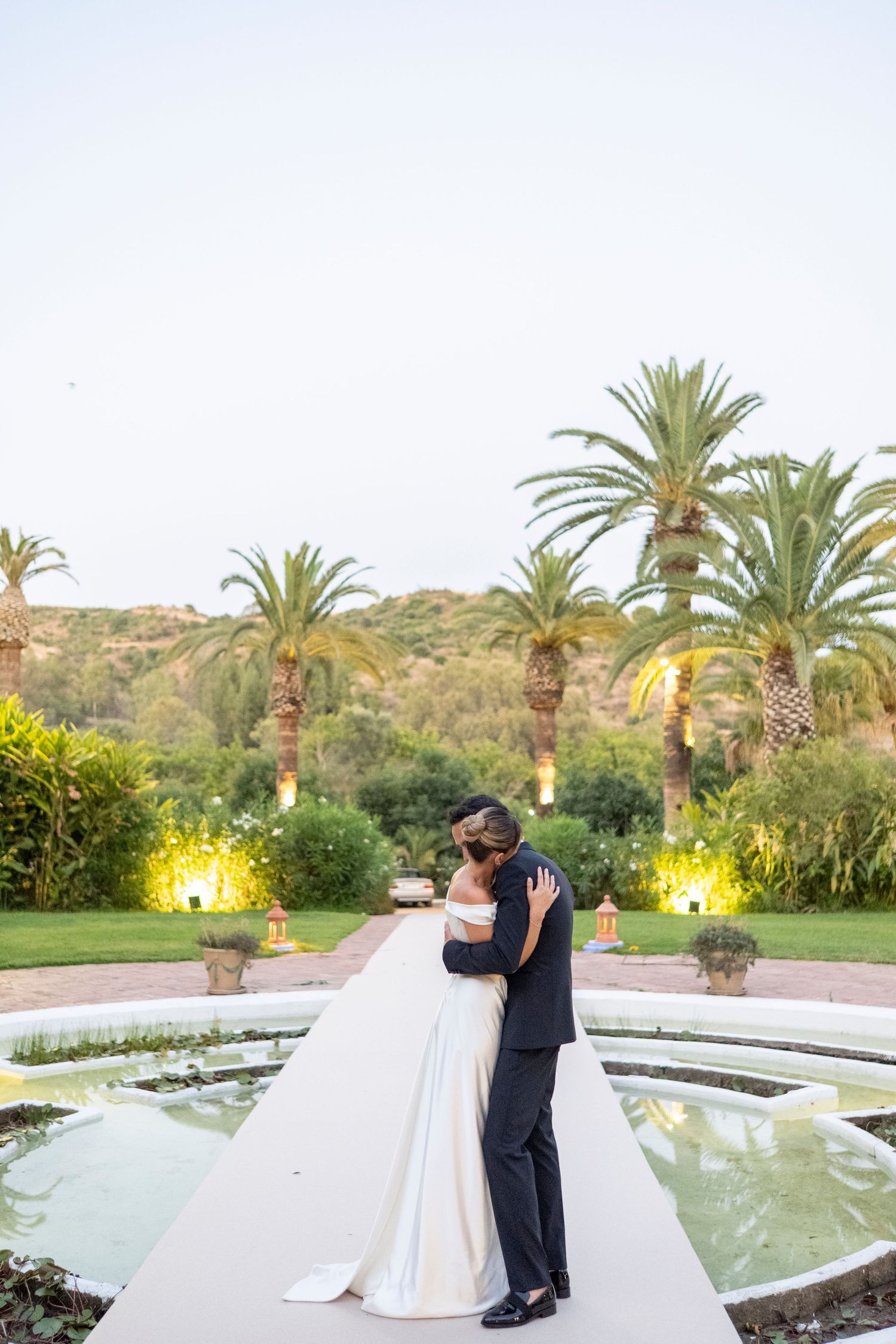 Evening wedding portraits by illuminated fountain with palm trees in background.