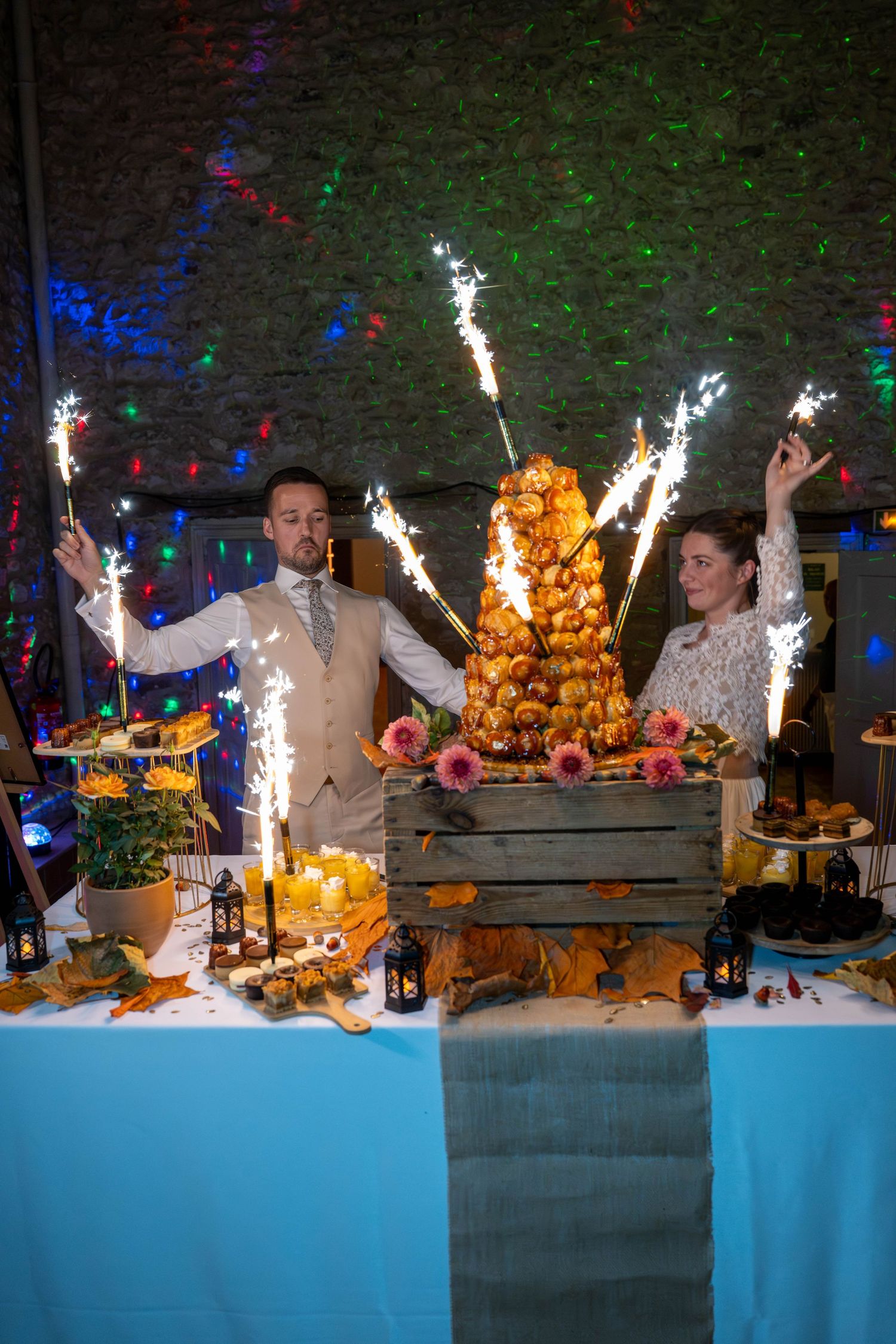 Wedding dessert table display with sparklers and colorful lighting effects.