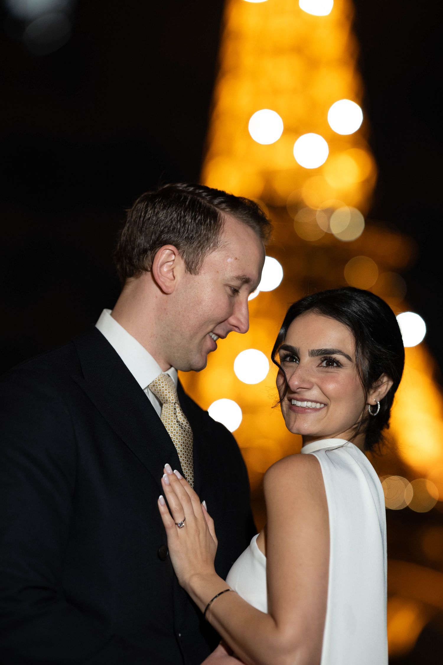 A couple shares an intimate moment on their wedding night with warm glowing lights in the background.