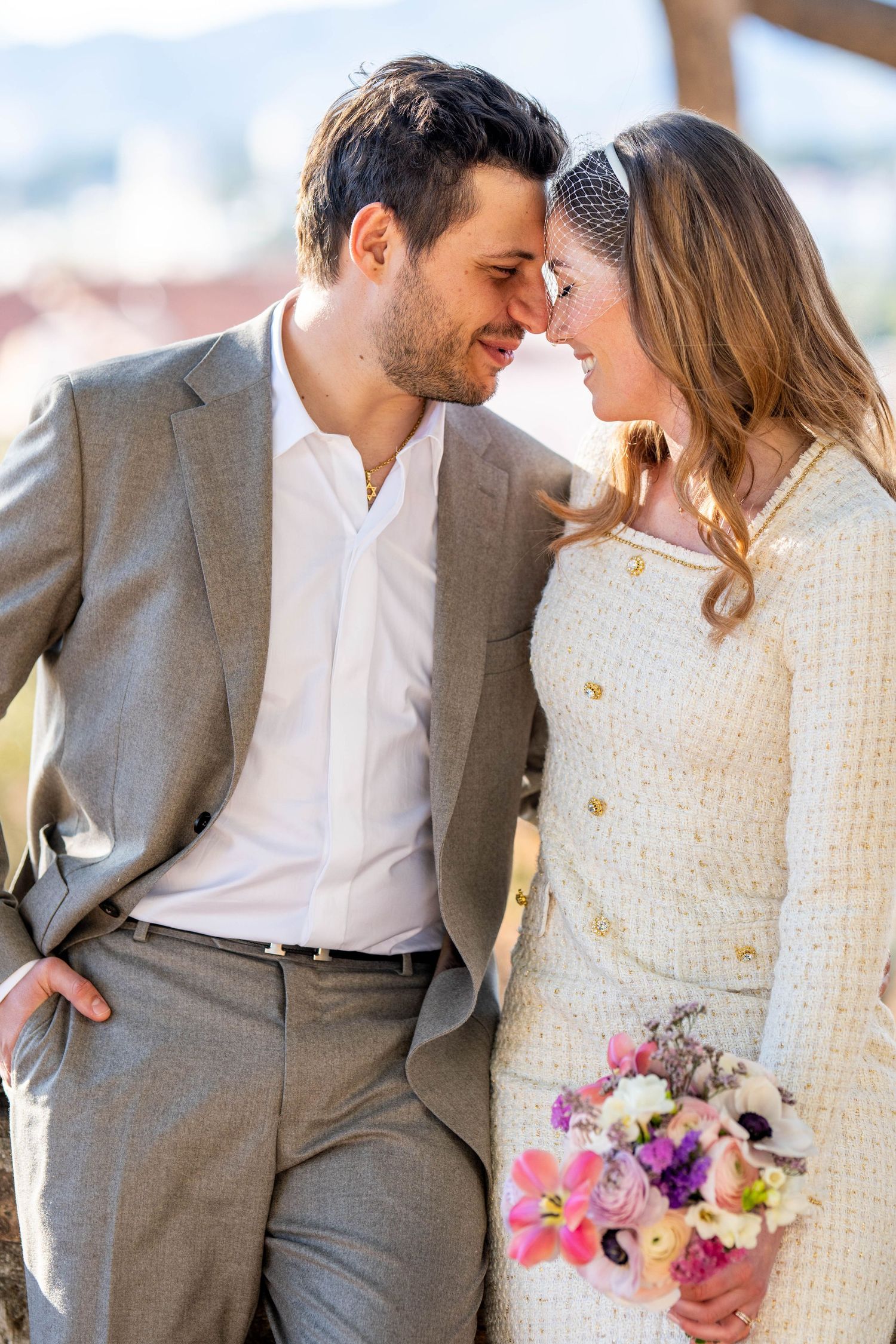 A romantic couple in gray suit and white dress share intimate moments while holding a colorful floral bouquet.