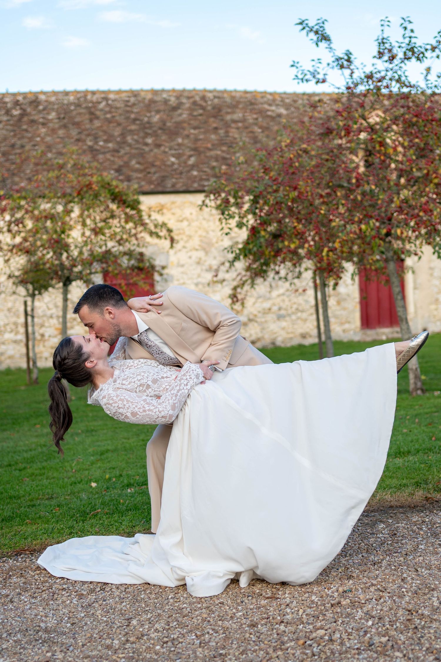 Wedding couple poses for romantic photos on grassy grounds near stone wall and red flowers.
