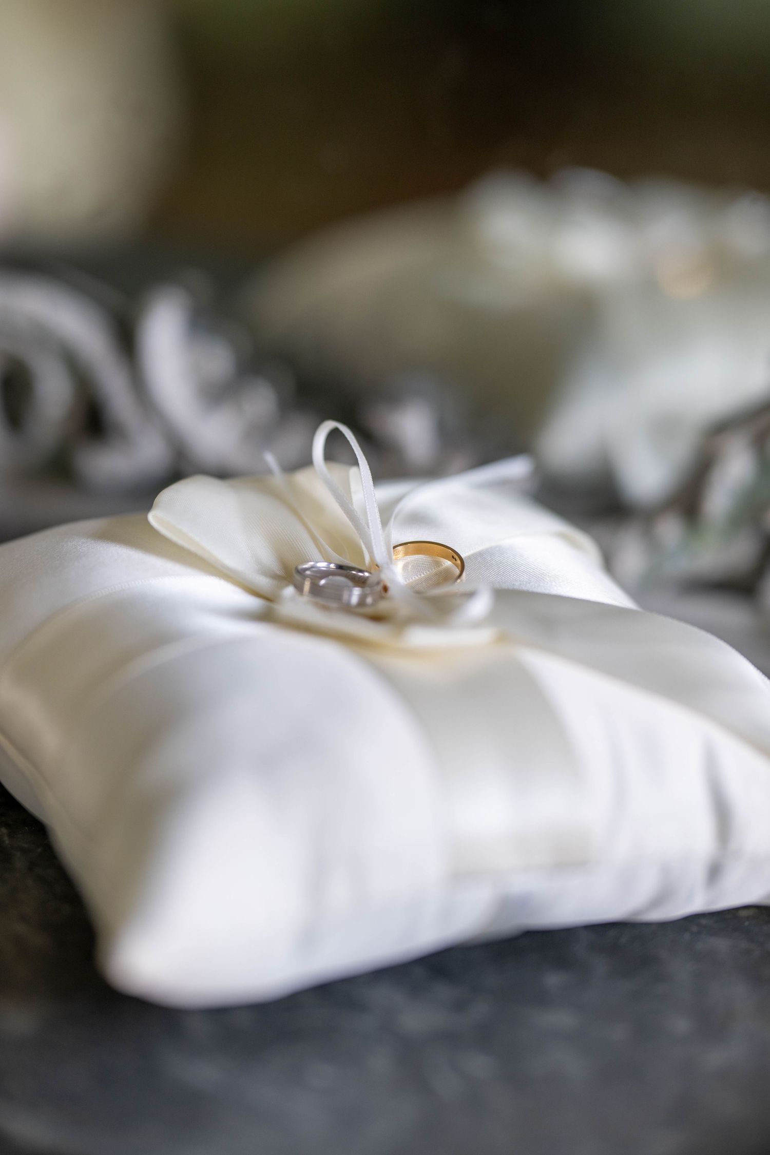 Wedding rings rest delicately on a white satin pillow in an artistic macro shot.