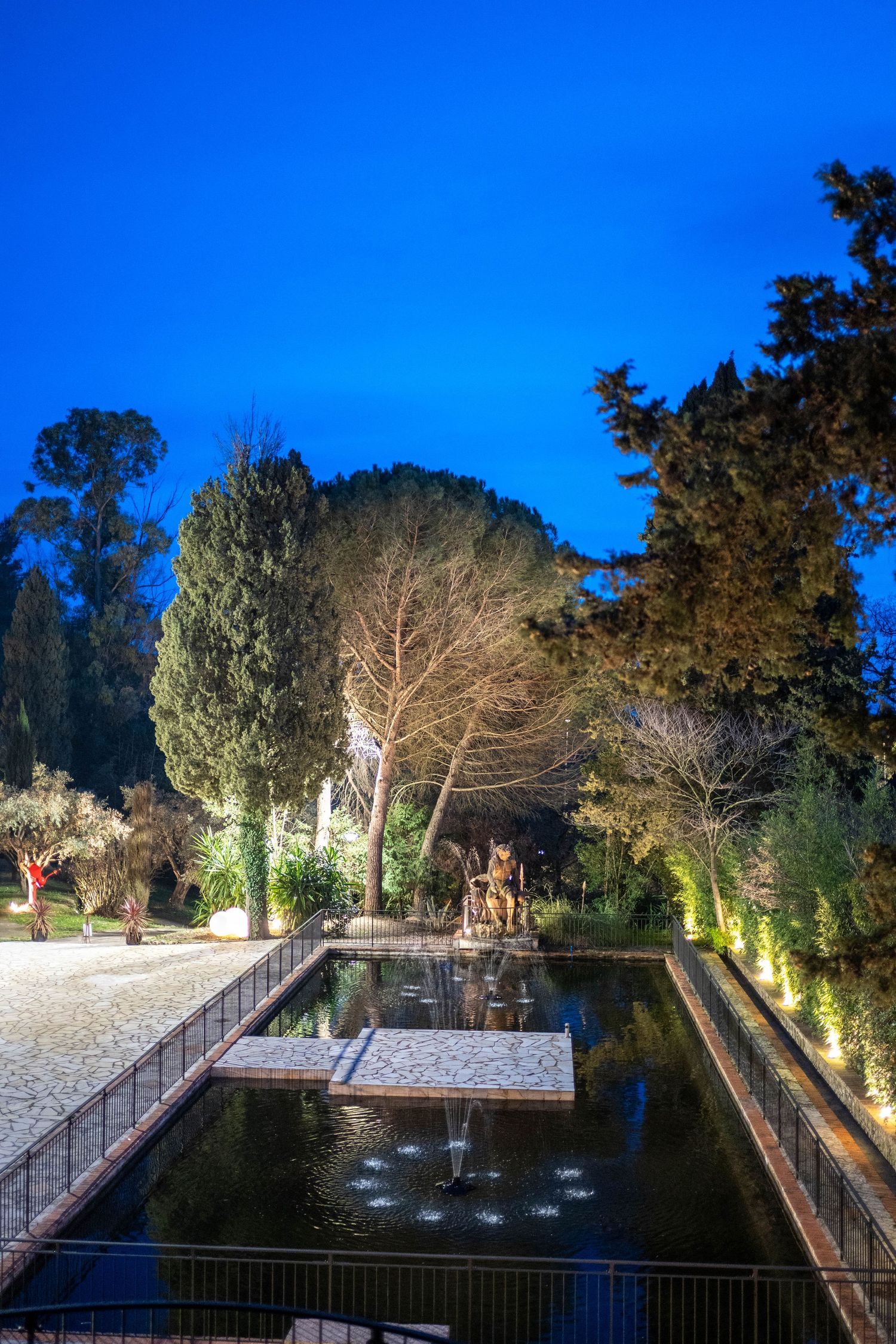 Illuminated formal garden with reflecting pool and fountains at night.