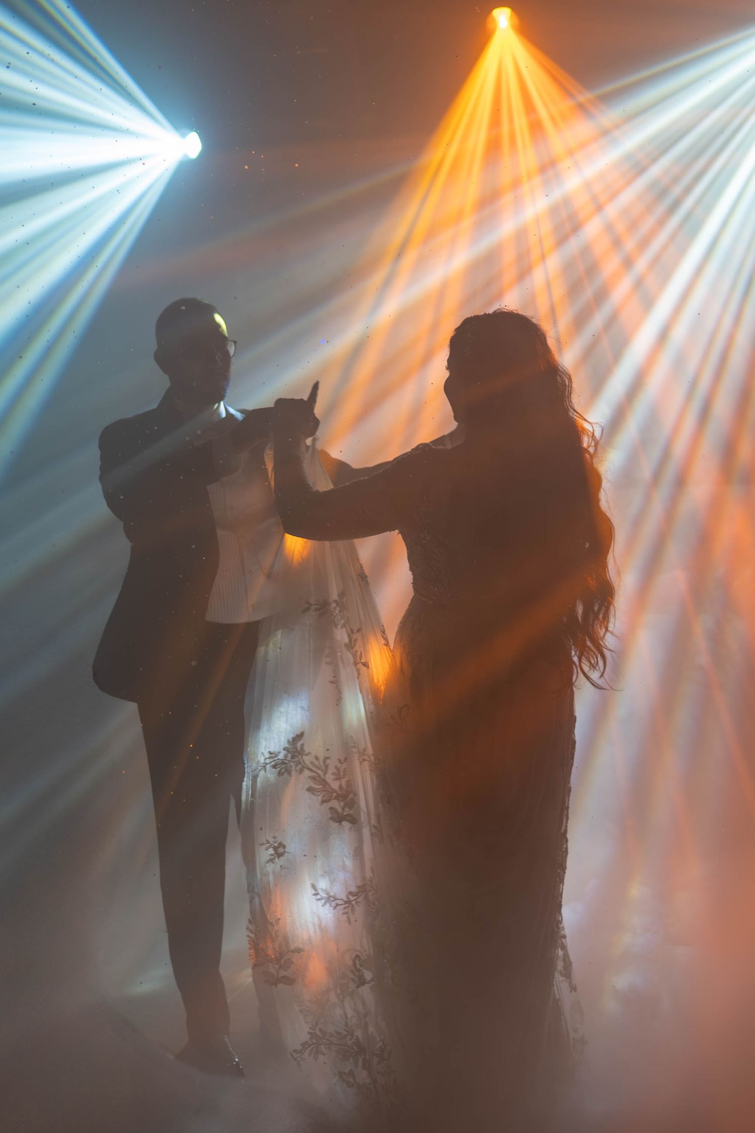 Dramatic silhouettes dance in atmospheric lighting with orange and white spotlights.