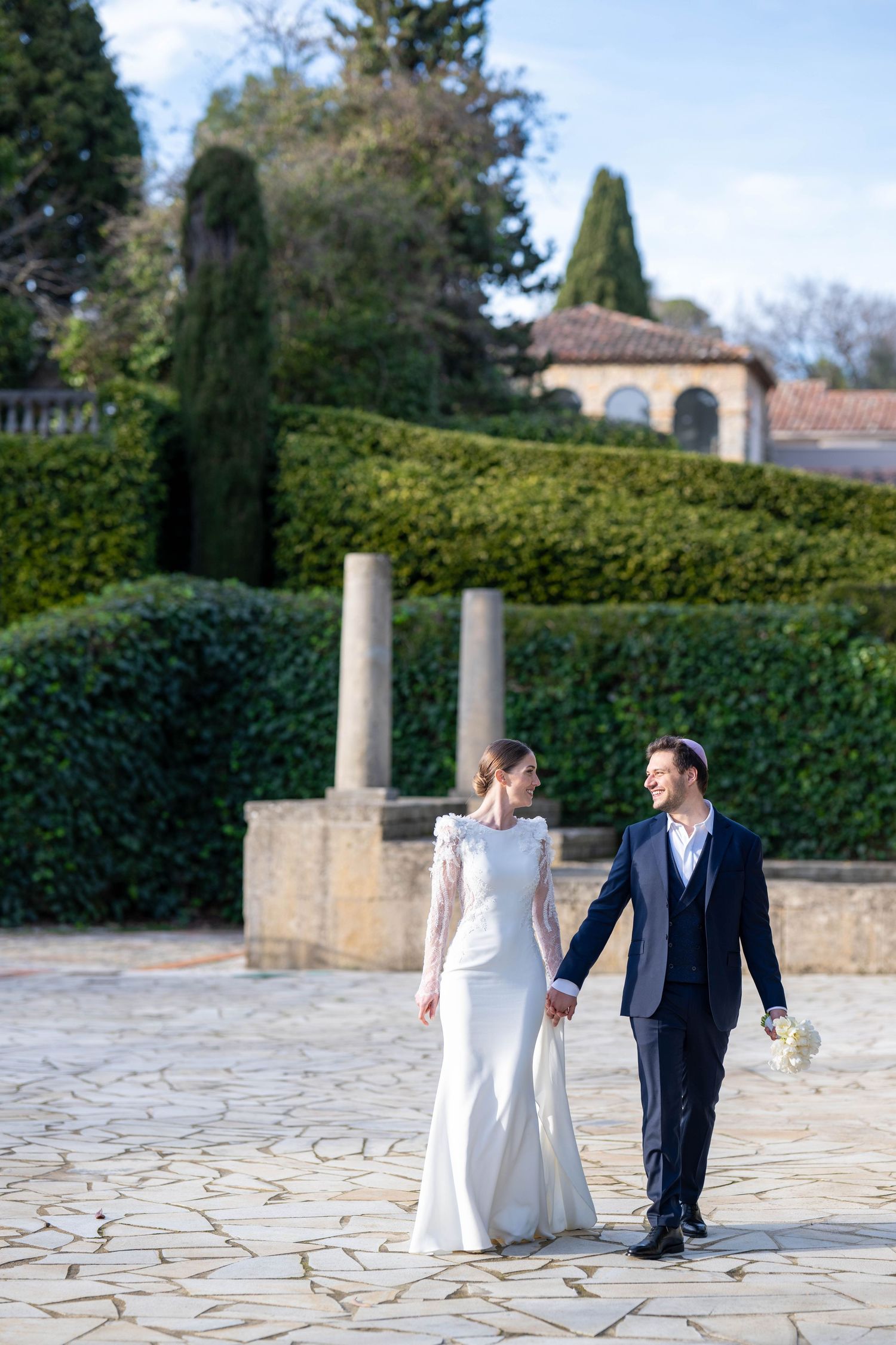 Couple in wedding attire strolling across stone paved courtyard.