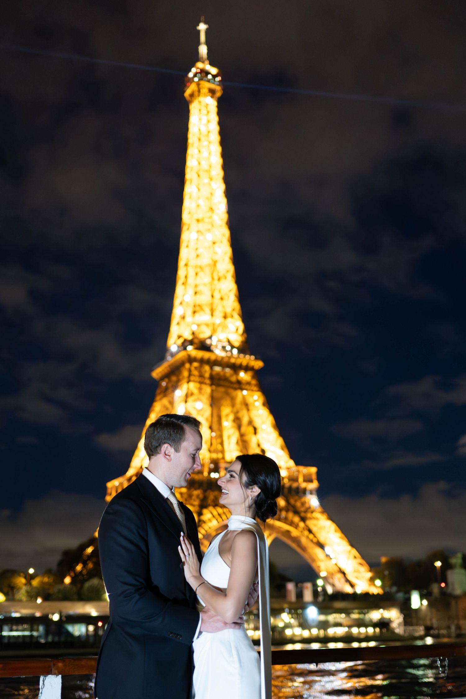 Couple sharing an intimate moment in front of the illuminated Eiffel Tower at night.