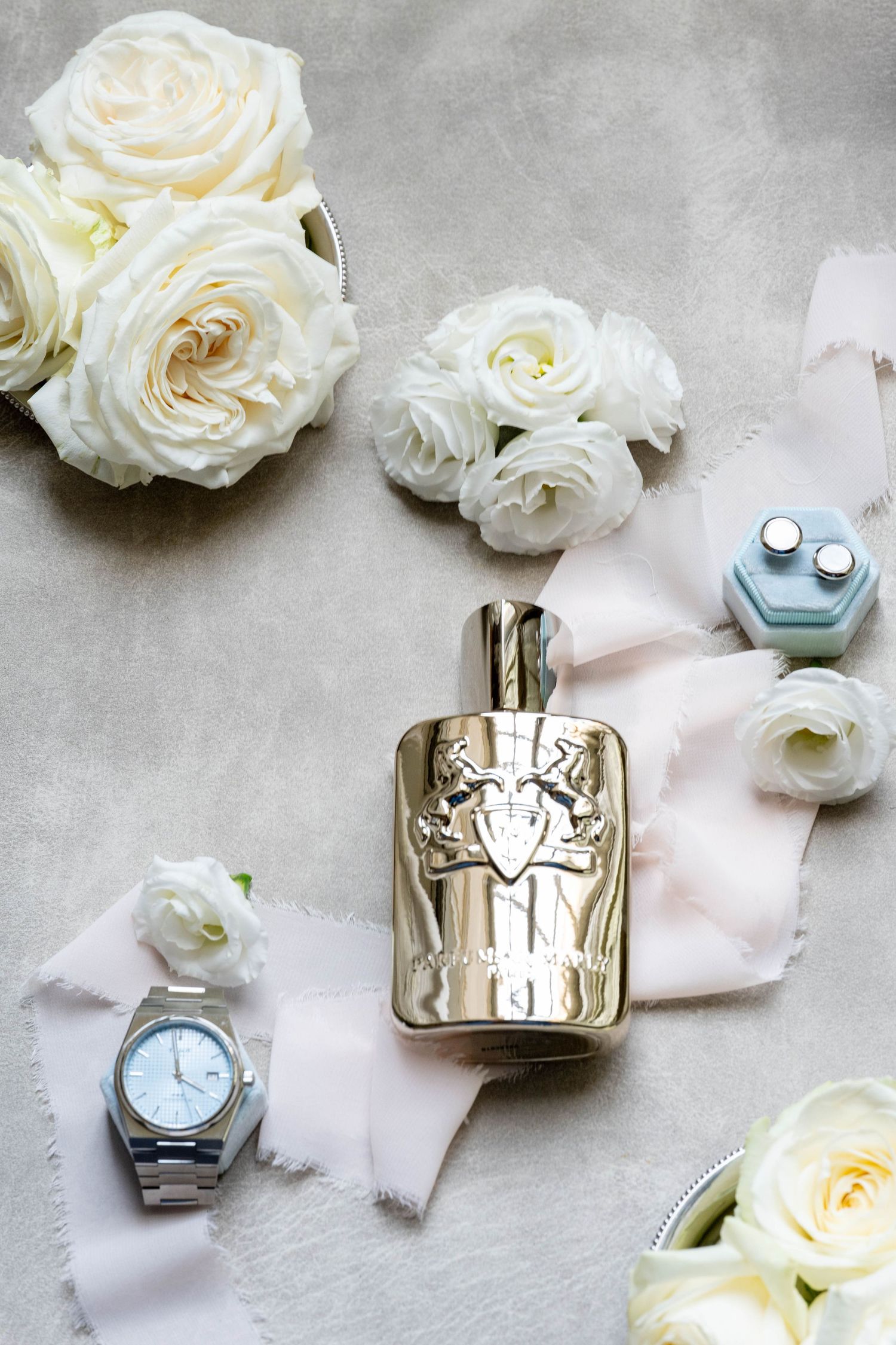 Luxury perfume bottles arranged with white roses on a light gray surface.