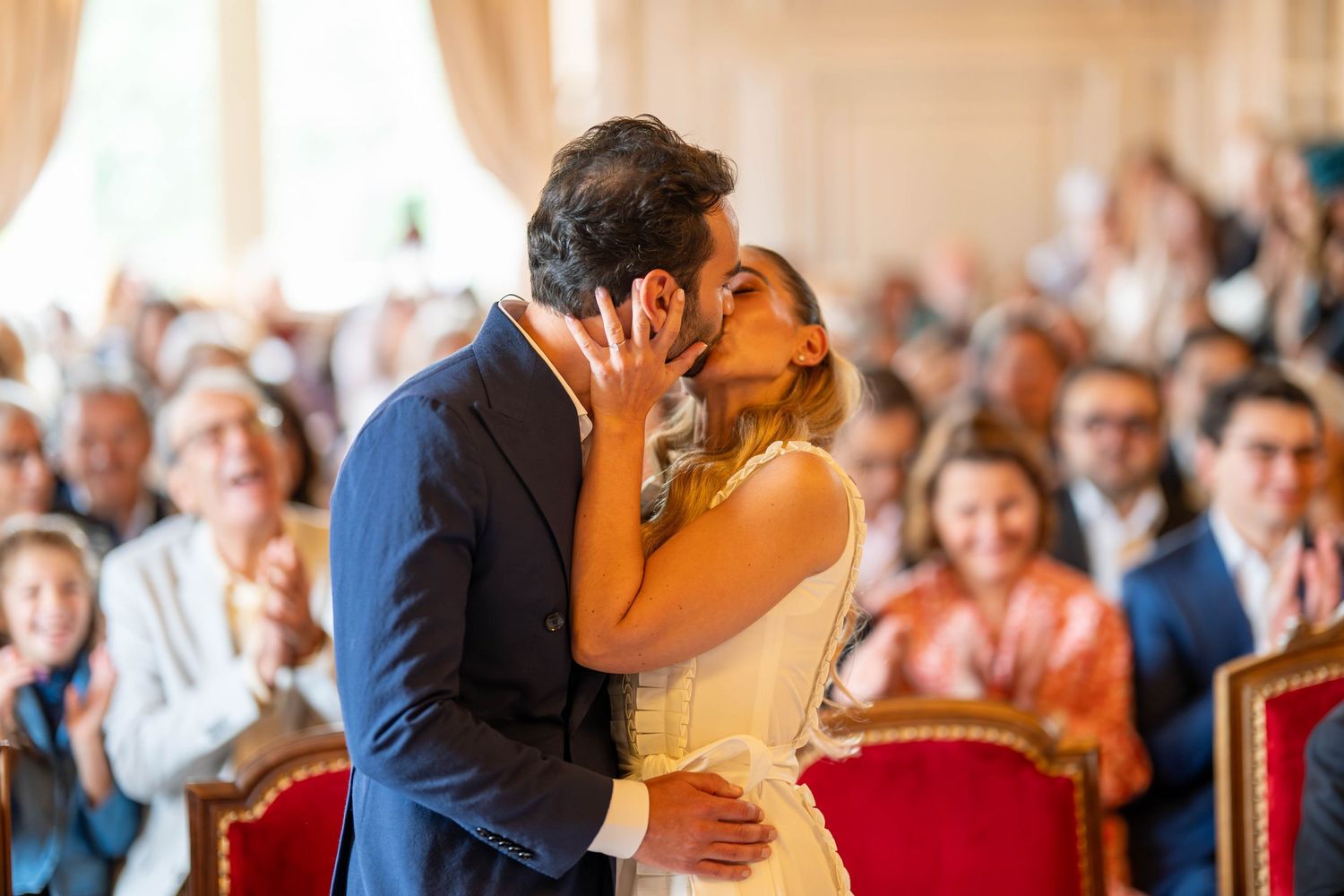 A couple shares their first dance at a wedding reception while guests look on and applaud in the background.