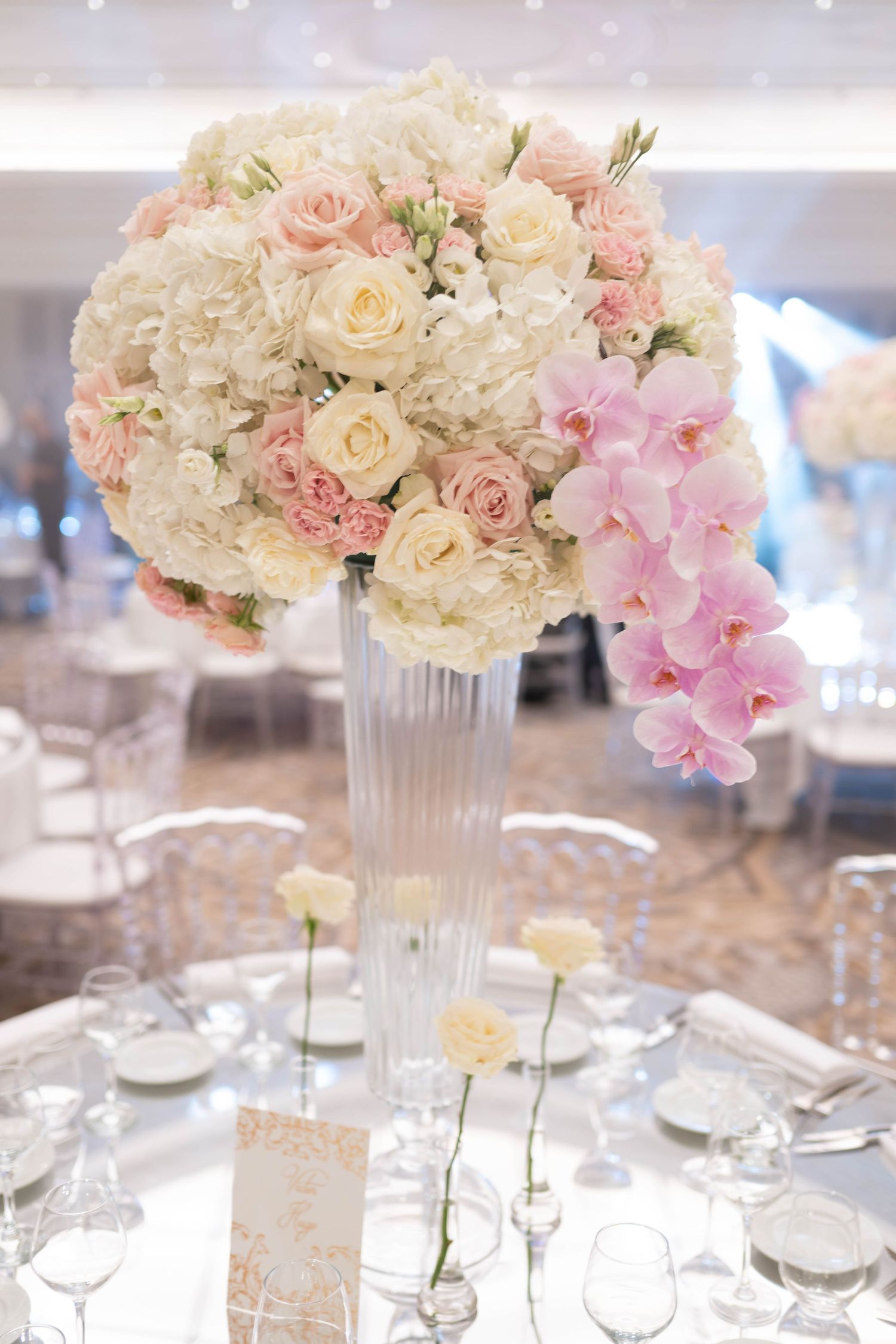 Elegant wedding centerpieces with pink and white roses in crystal vases on reception tables.