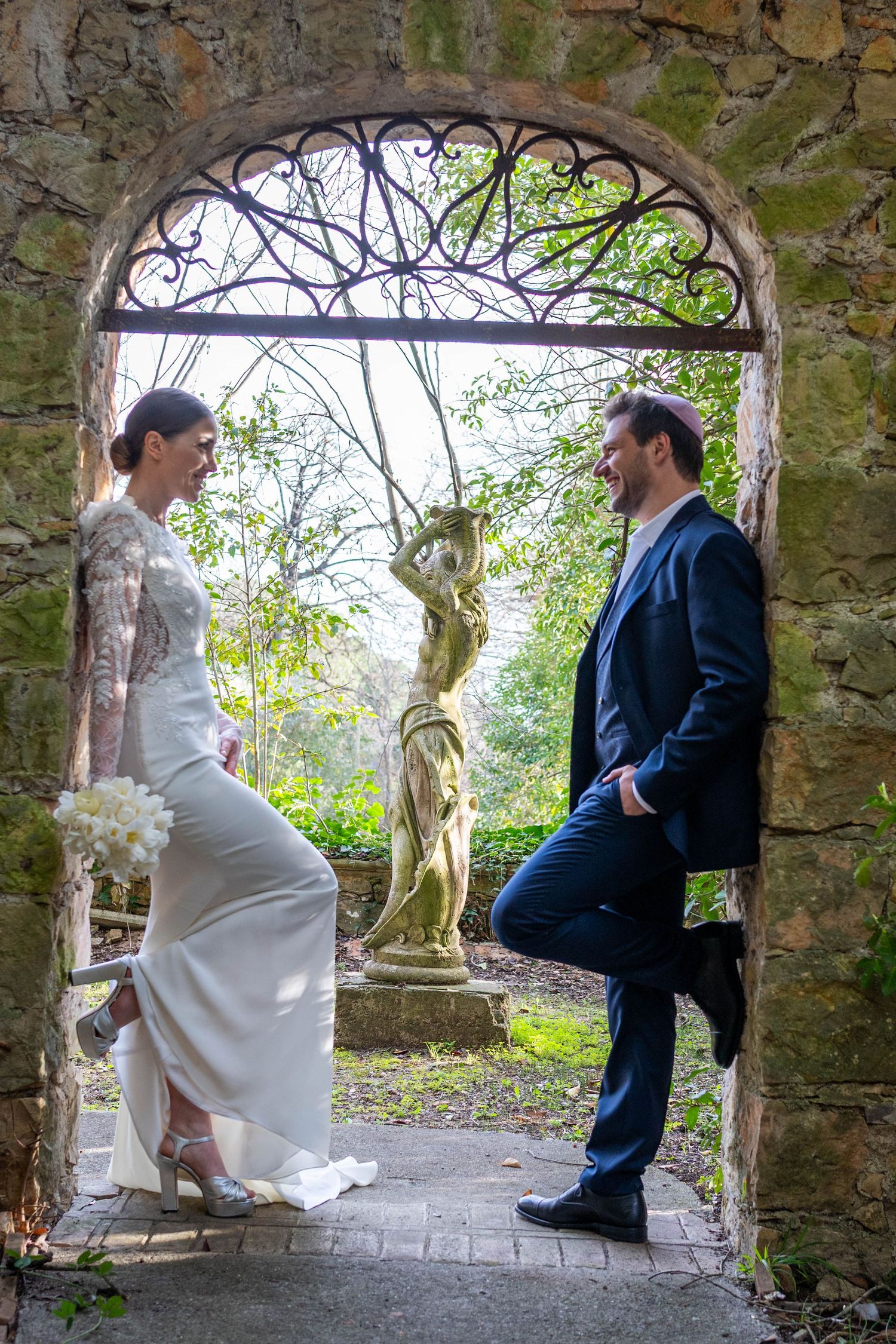 Wedding couple poses in rustic stone archway with natural garden backdrop.