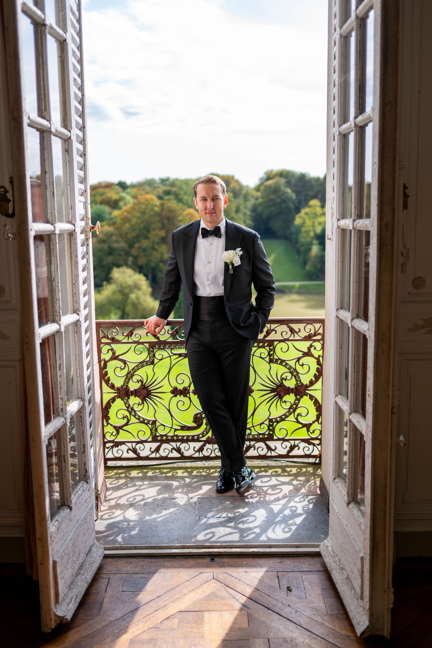 Elegant French doors open to a balcony with ornate wrought iron railings overlooking a scenic countryside estate.