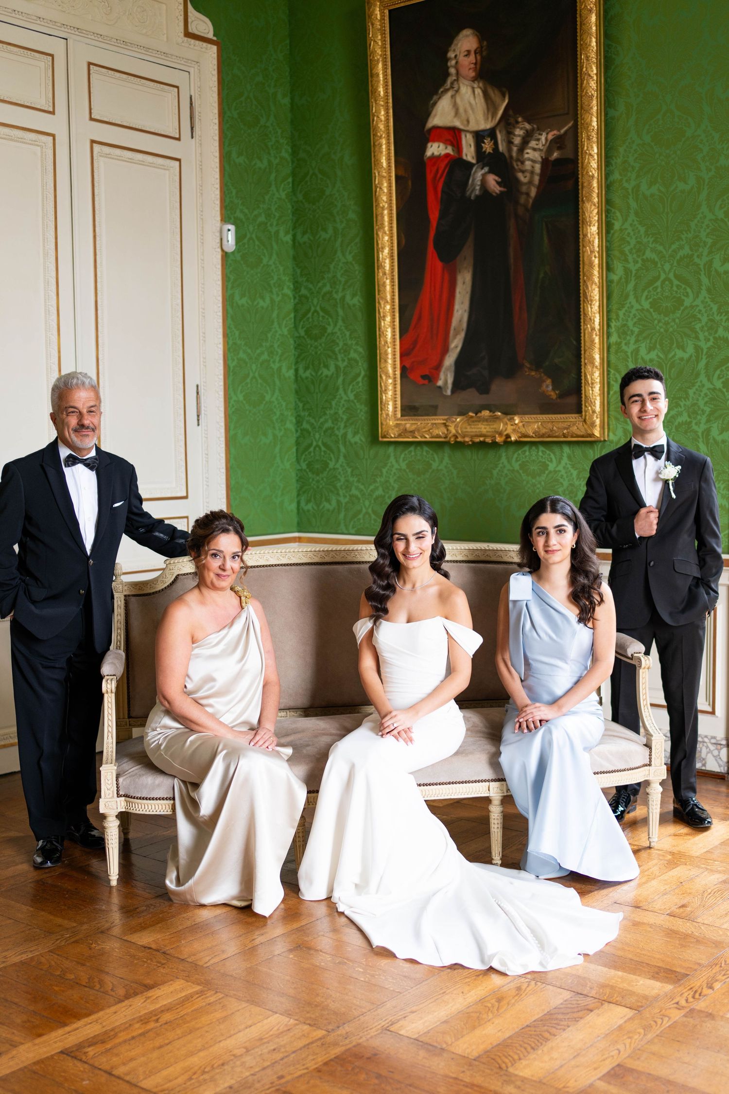 Bridesmaids in light blue dresses sit elegantly on a floor against green wallpapered walls.